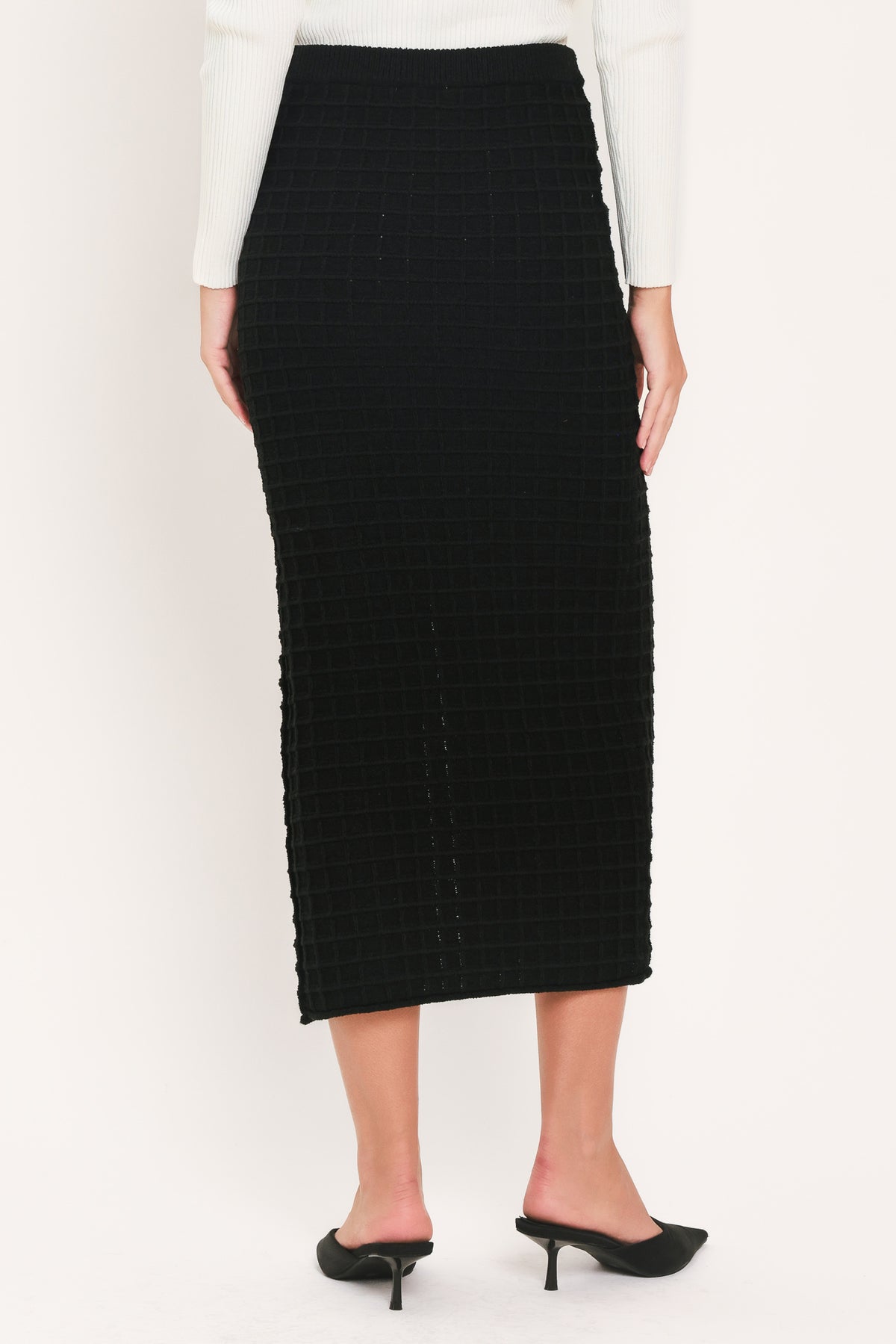 A black textured midi skirt with a front slit and three decorative silver buttons, worn by a model | Flying Tomato