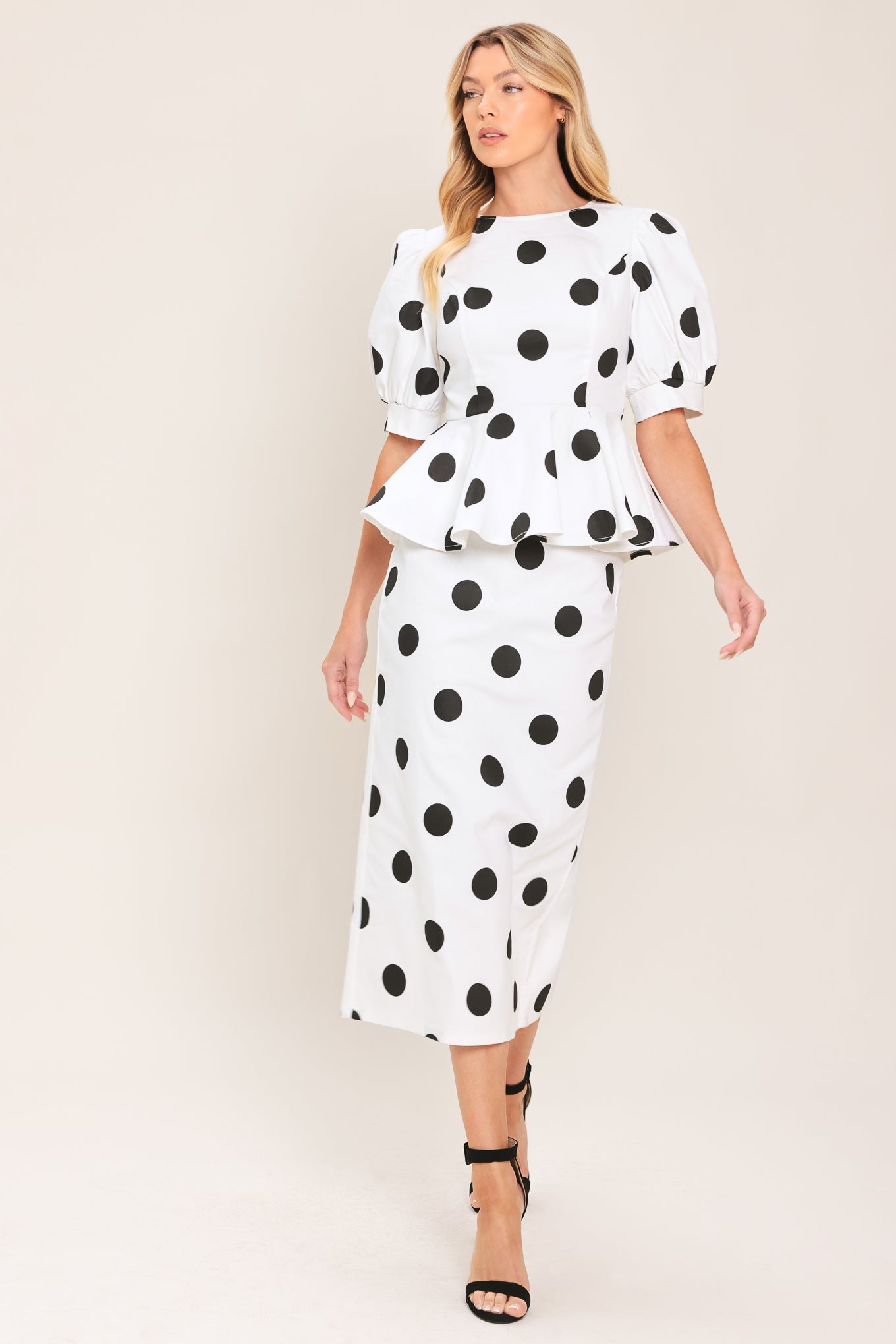 A woman wearing a white midi pencil skirt and matching top with large black polka dots, featuring short puff sleeves and a peplum waist | Flying Tomato