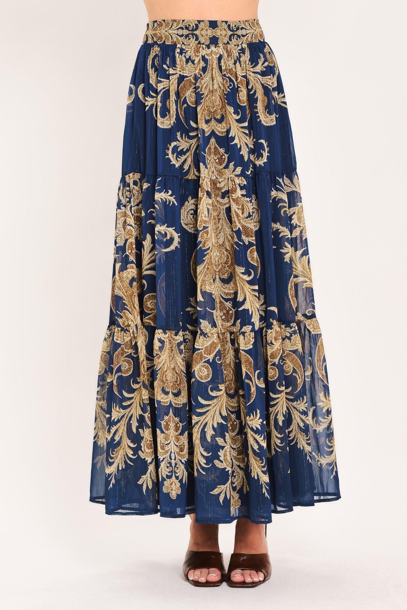 A navy blue tiered maxi skirt with an ornate gold and brown baroque damask pattern, shown on a model | Flying Tomato