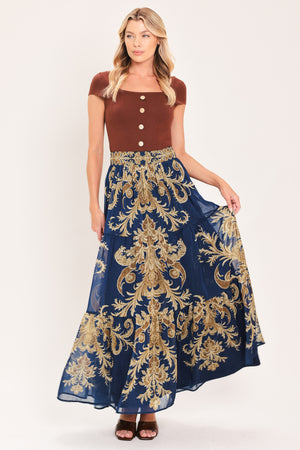A navy blue tiered maxi skirt with an ornate gold and brown baroque damask pattern, shown on a model | Flying Tomato