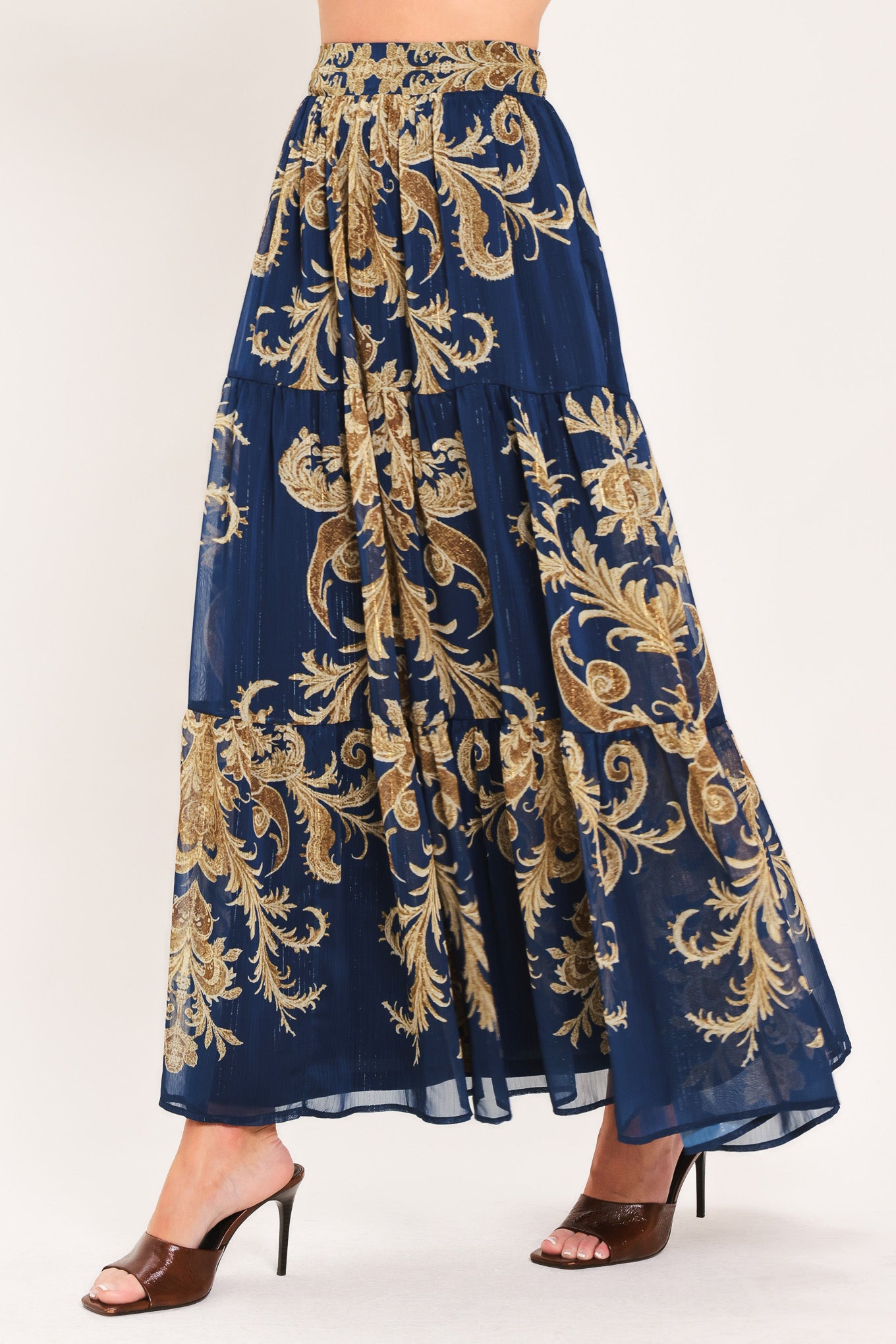 A navy blue tiered maxi skirt with an ornate gold and brown baroque damask pattern, shown on a model | Flying Tomato