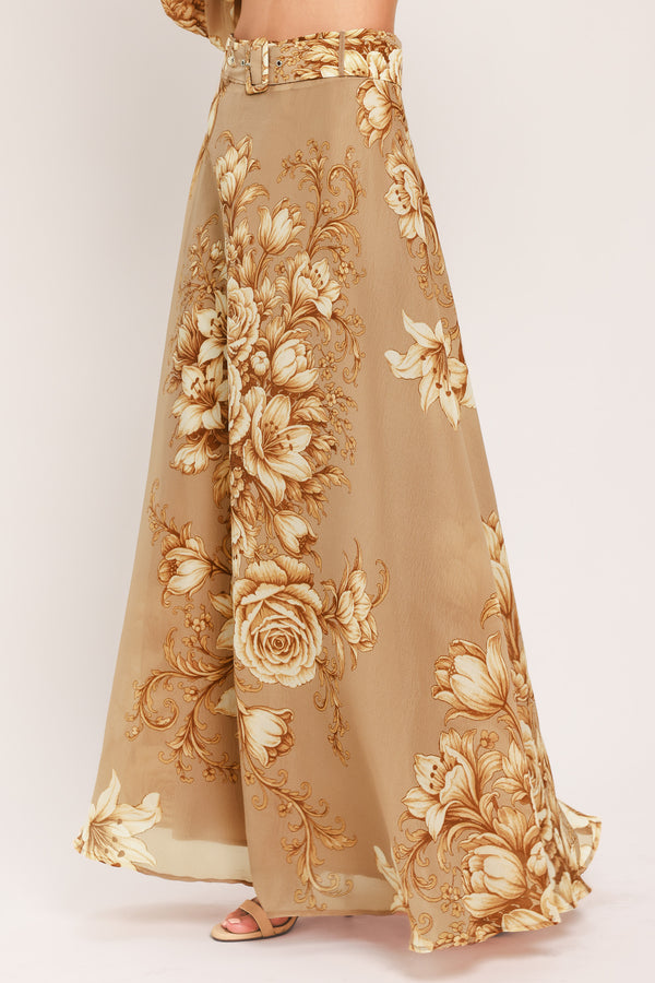 A floor-length beige skirt with a large gold and cream floral rose pattern, featuring a matching beaded belt, shown on a model | Flying Tomato