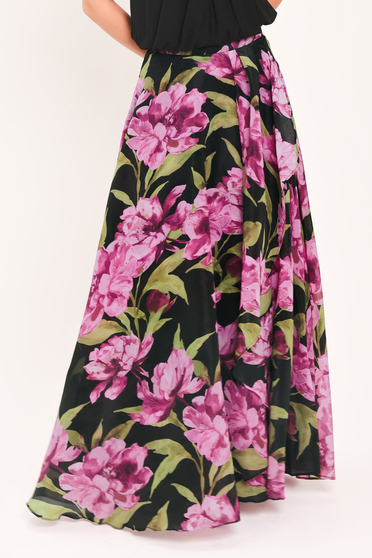 A black maxi skirt with a large pink floral print and green leaves, shown on a model | Flying Tomato
