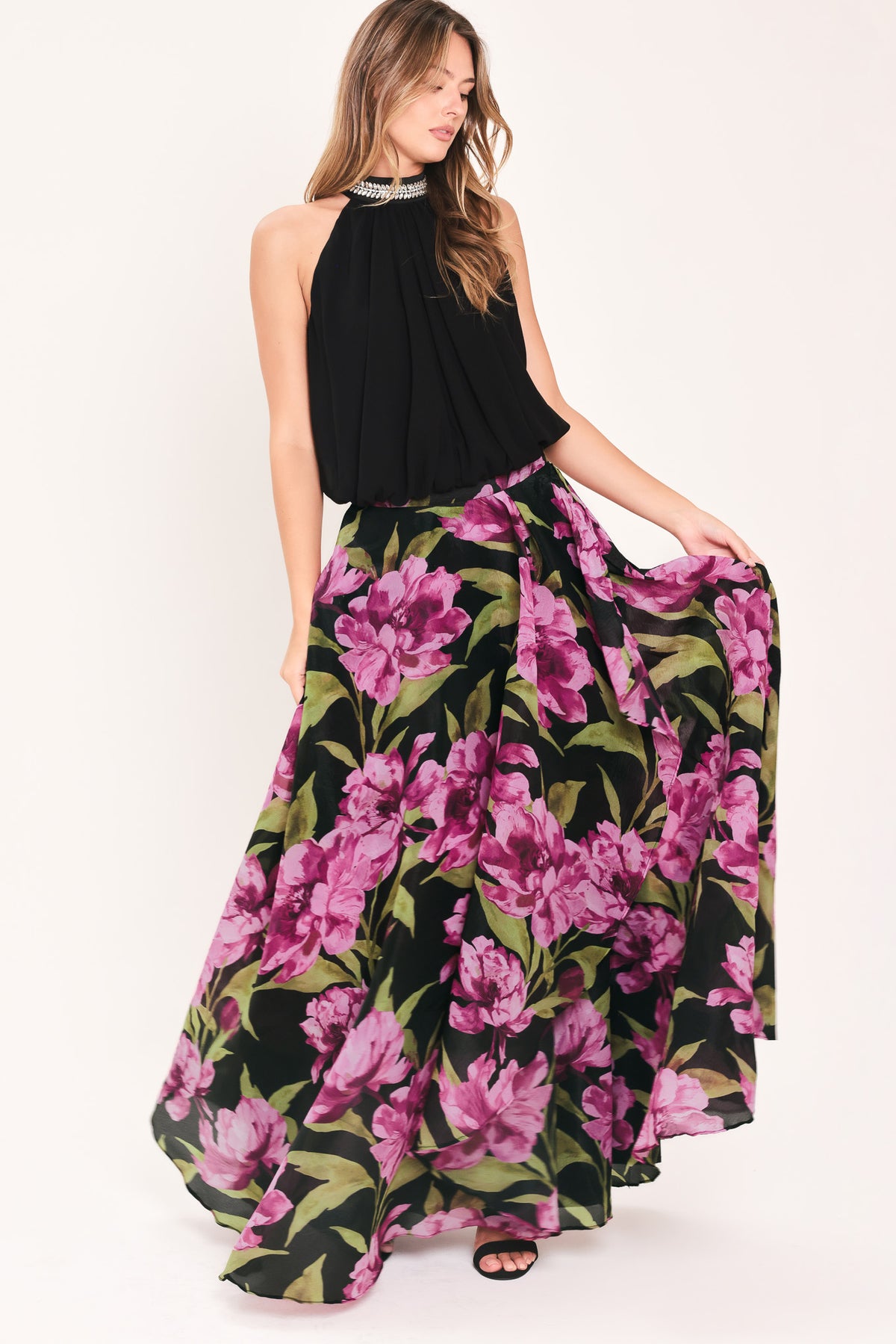 A black maxi skirt with a large pink floral print and green leaves, shown on a model | Flying Tomato