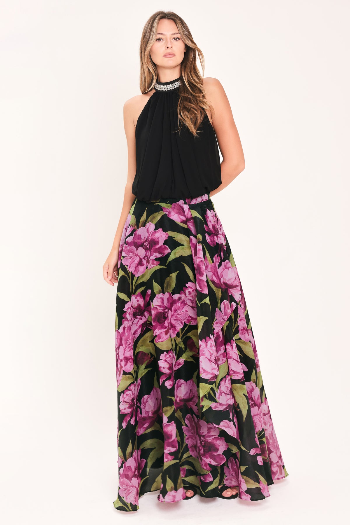 A black maxi skirt with a large pink floral print and green leaves, shown on a model | Flying Tomato