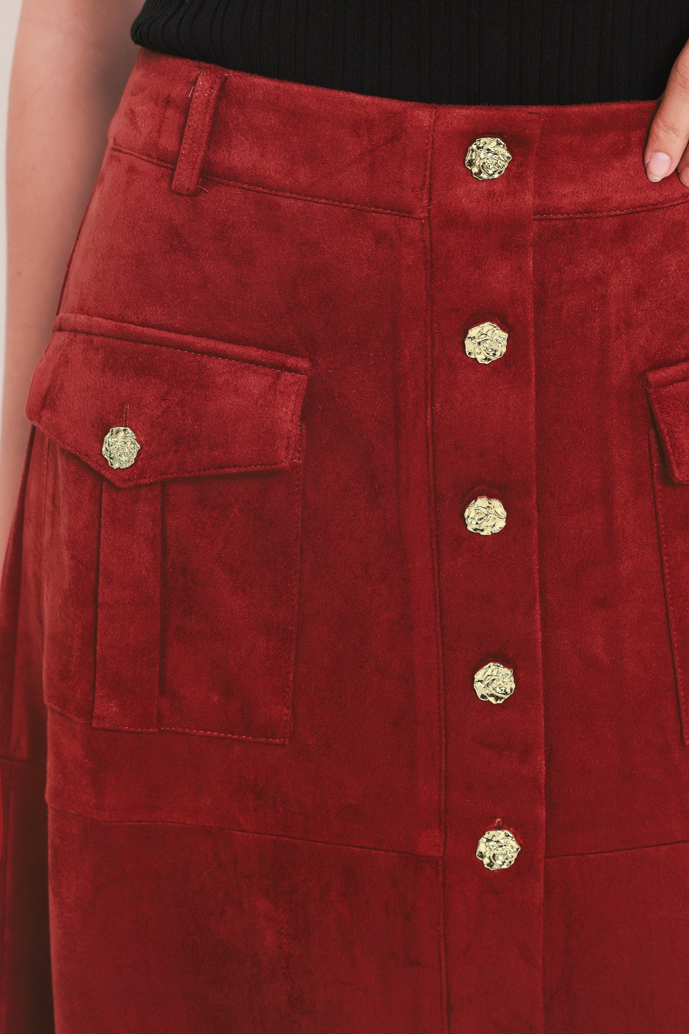 A brick colored suede midi skirt with a button-down front, flap pockets, and gold-tone button accents, shown on a model | Flying Tomato