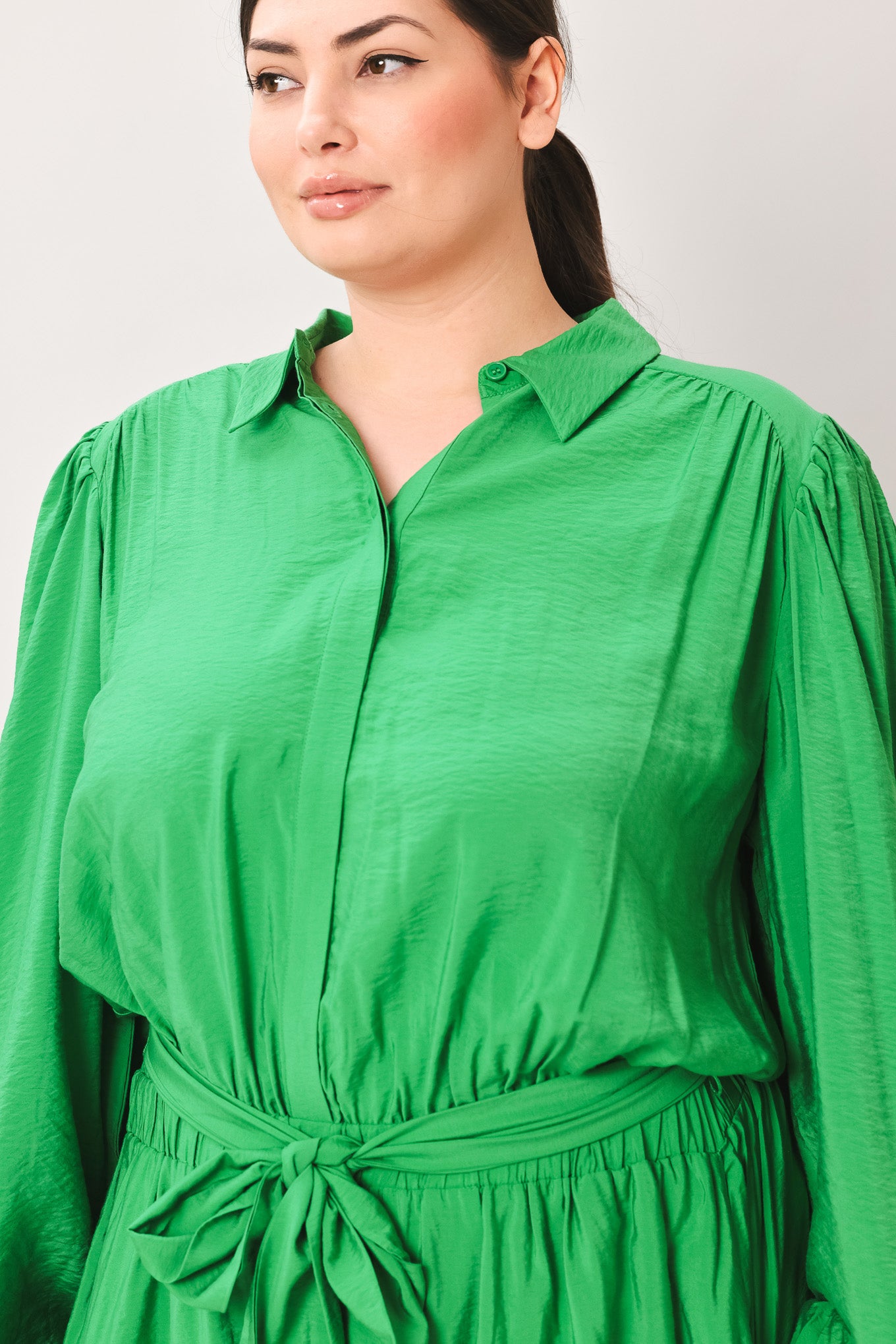Woman wearing a green jumpsuit featuring shirt collar, button down, long sleeve, elasticized waist, self sash tie, side pockets and wide leg on a white background | Flying Tomato