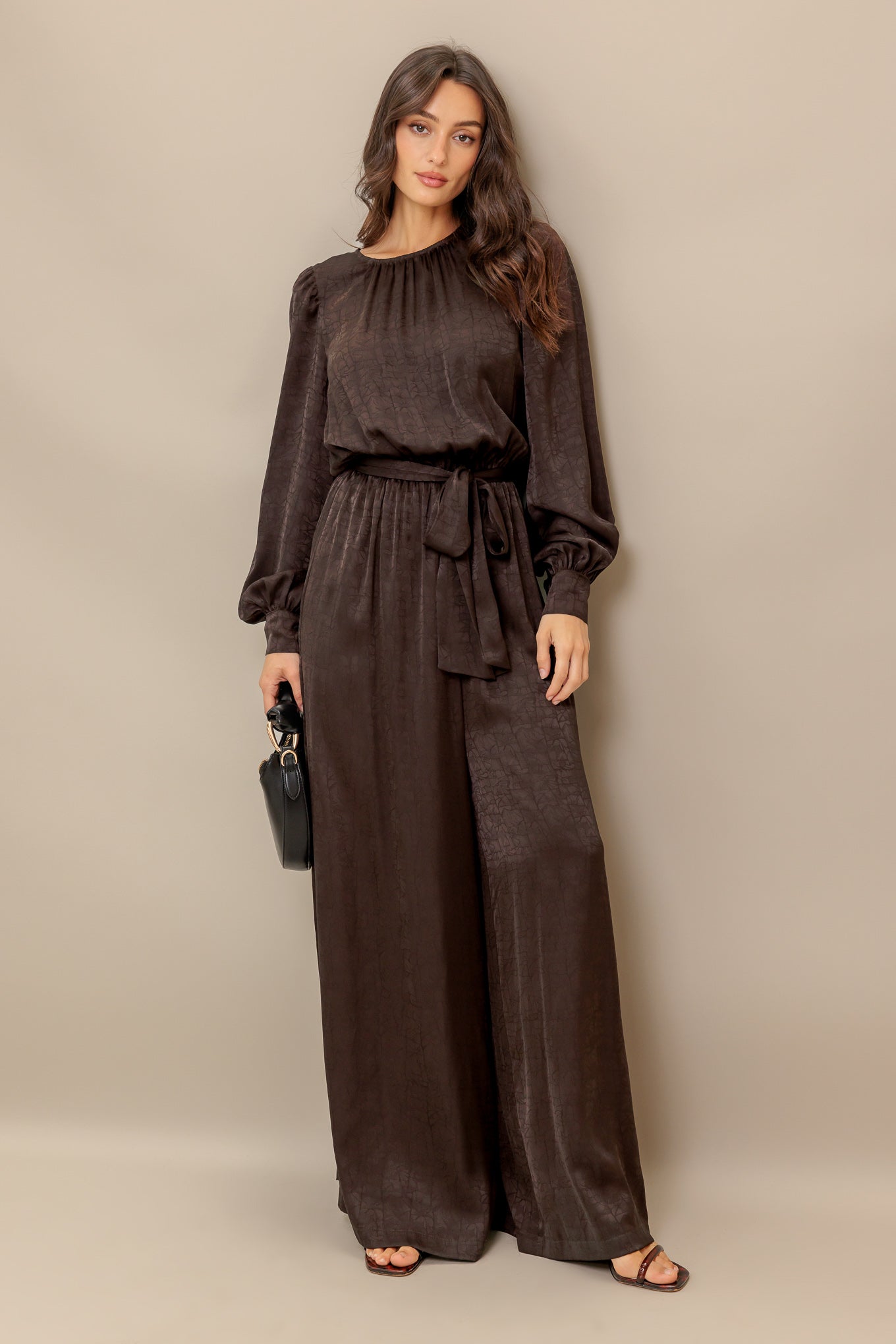 A solid woven jumpsuit featuring round neckline, long sleeve, elasticized waist with self sash tie, wide leg and split back with back neck button closure

Details:

Self : 97% Polyester, 3% Spandex

Size &amp; Fit

- Model is 5`8" And Wearing Size Small
- Measurements Taken From Size Small
- Approx. Length: 60"
- Approx. Inseam: 28"