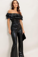Woman wearing a black off-shoulder top and high-waisted pants against a white background
