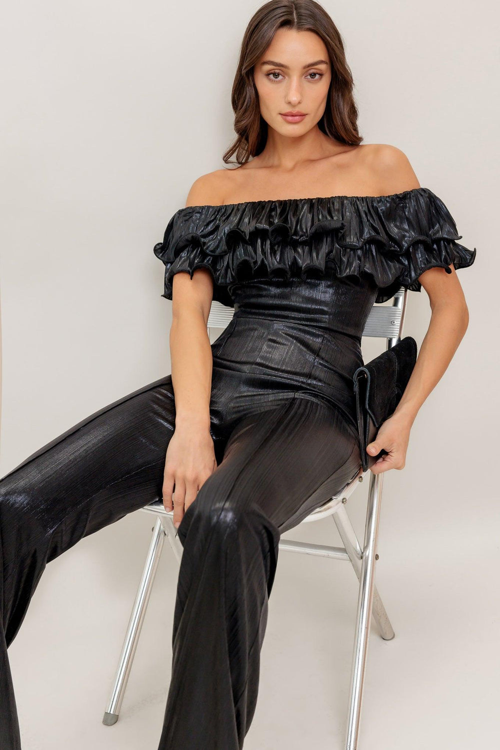 Woman wearing a black off-shoulder top and high-waisted pants against a white background