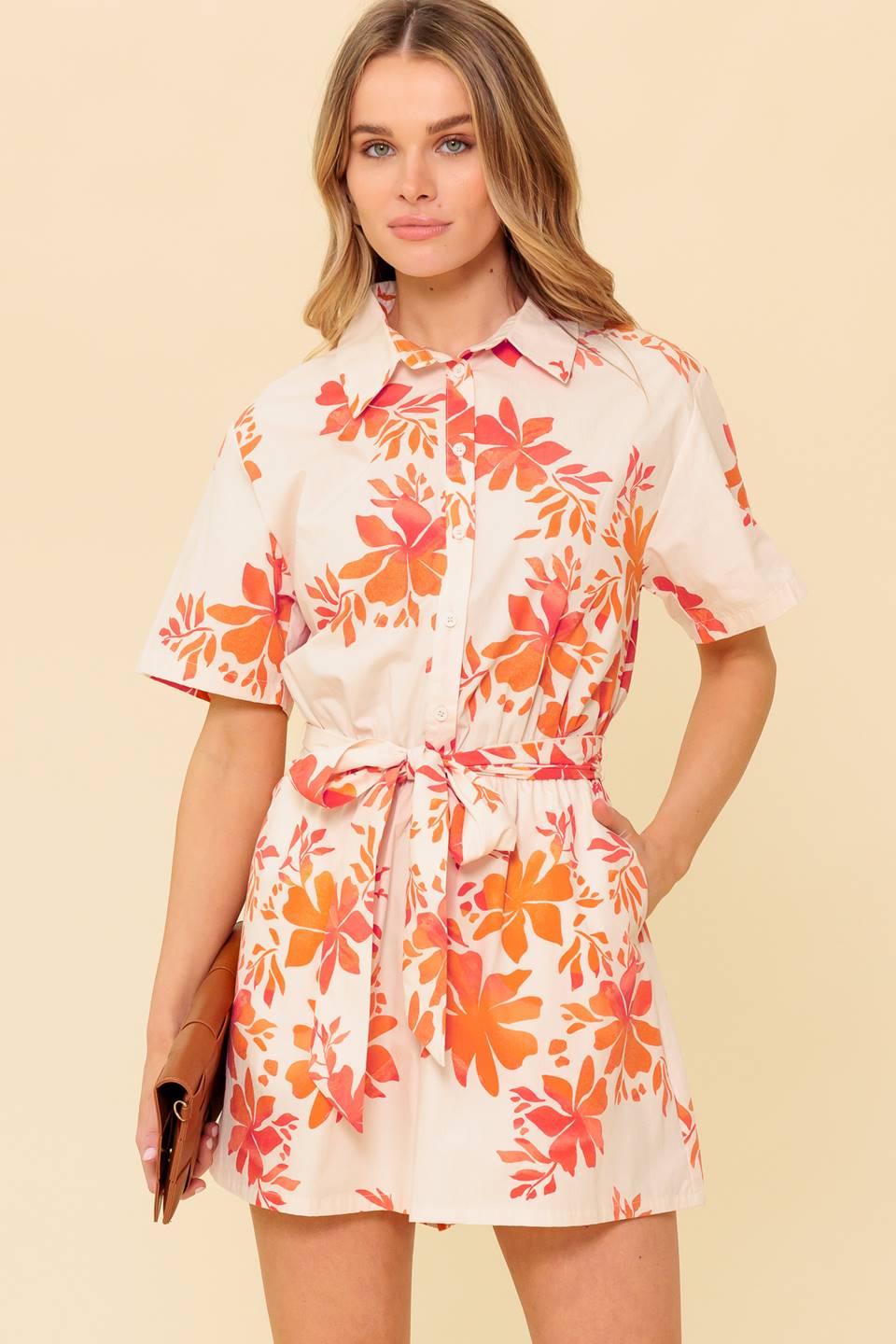 A printed woven romper featuring collar, button down, short sleeve, self sash tie and elasticized waist