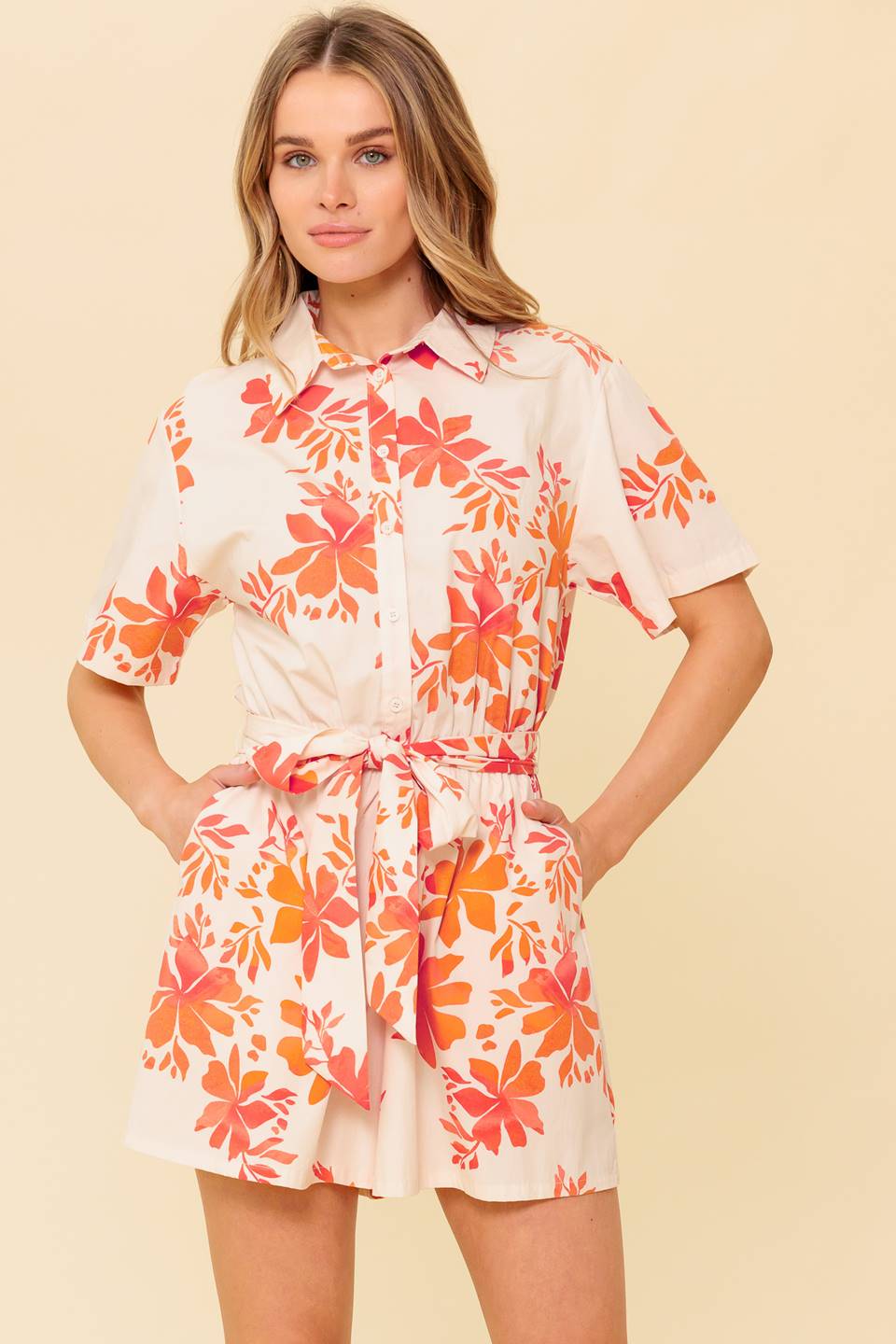 A printed woven romper featuring collar, button down, short sleeve, self sash tie and elasticized waist