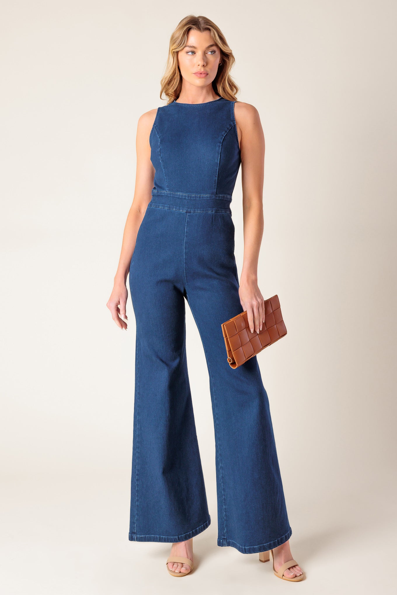 A washed stretch denim jumpsuit featuring round neckline, sleeveless, wide leg and bare back with heart shape cut out and zipper closure.