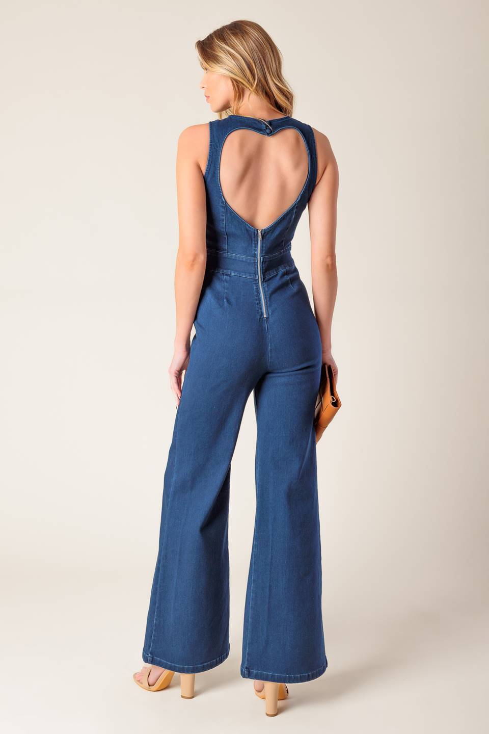 A washed stretch denim jumpsuit featuring round neckline, sleeveless, wide leg and bare back with heart shape cut out and zipper closure.