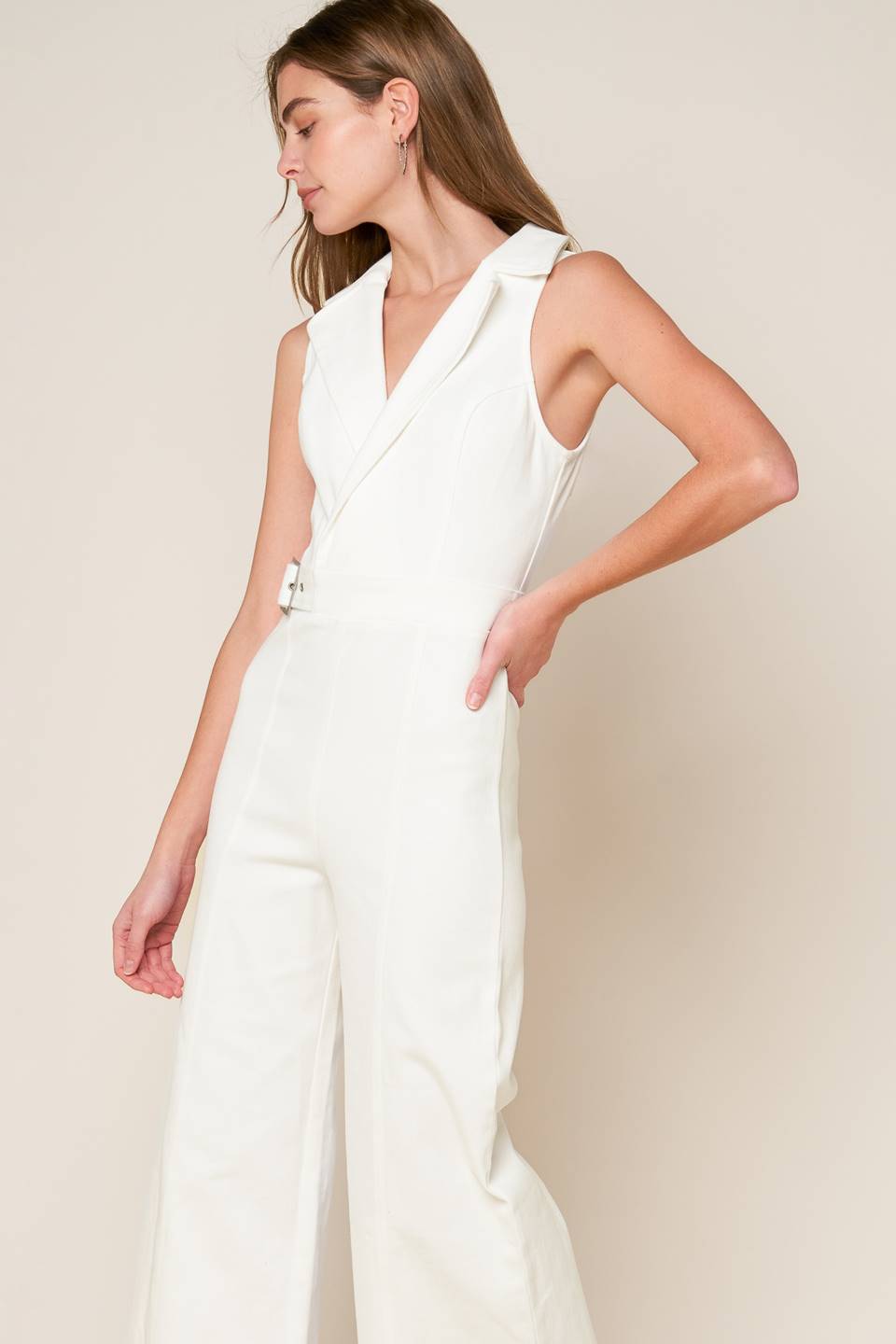 A sleeveless solid white woven jumpsuit featuring surplice neckline with collar, attached side belt, wide leg and back zipper closure.