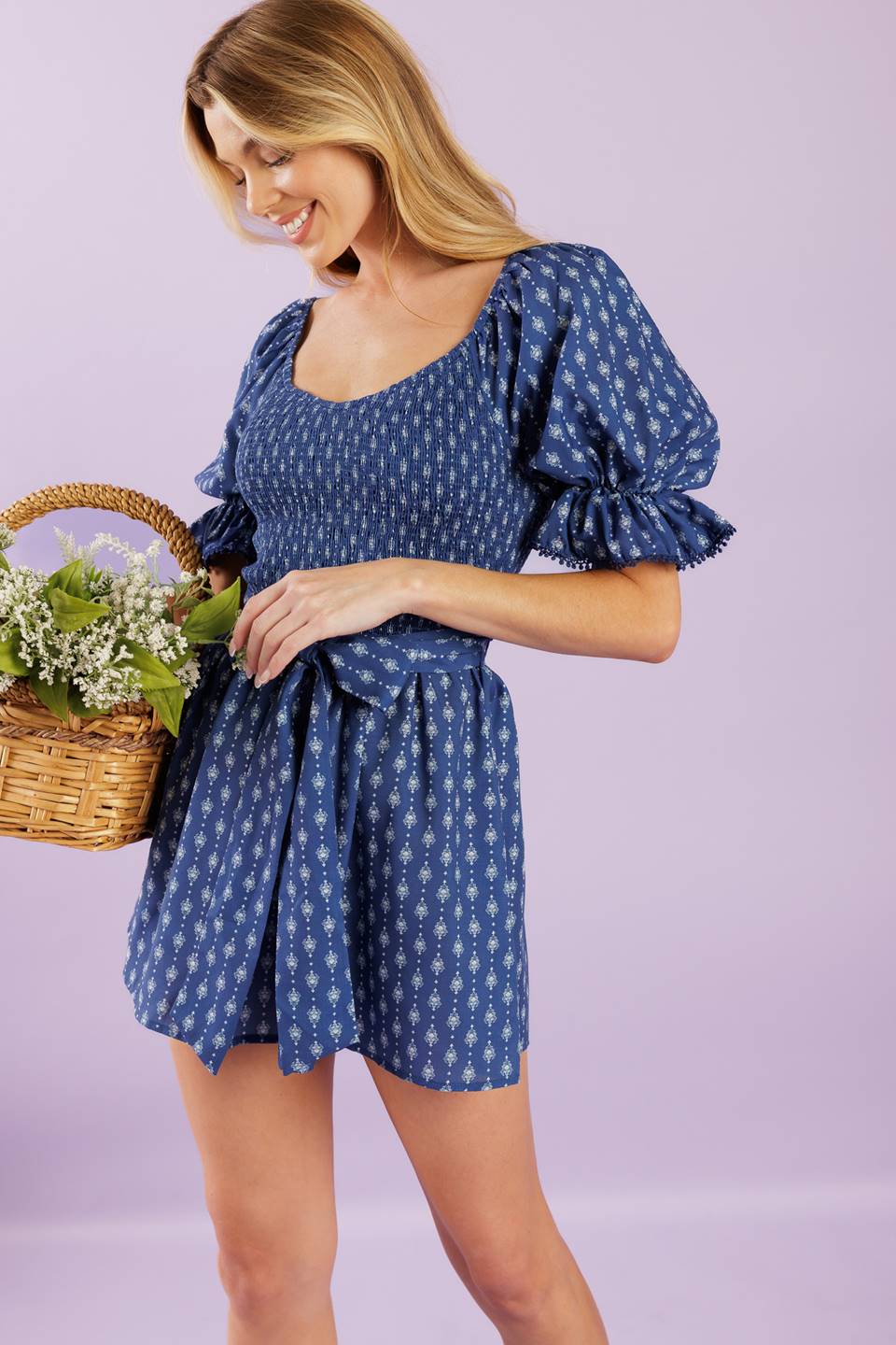 A textured woven romper featuring sweetheart neckline, short sleeve with lace trimmed ruffled cuff, smocked bodice, self sash belt and lace trimmed hemline.