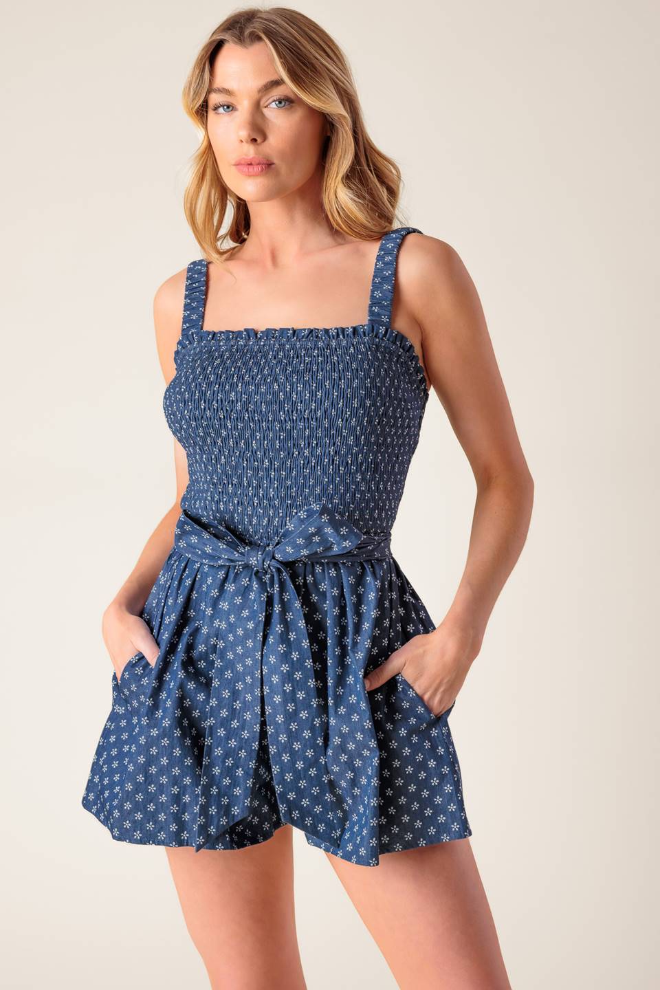 A textured woven romper featuring straight neckline, straps, smocked bodice, self sash tie and short.