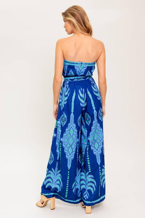 A printed woven jumpsuit featuring strapless, self sash tie, wide leg and back zipper closure