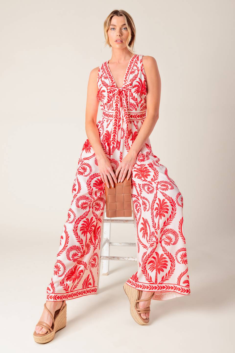 A white and red printed woven jumpsuit featuring V neckline with front tie, sleeveless, wide leg and back zipper closure.