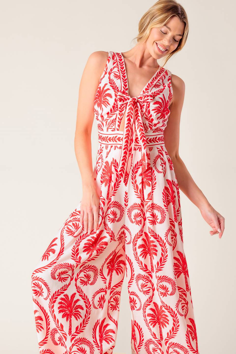 A white and red printed woven jumpsuit featuring V neckline with front tie, sleeveless, wide leg and back zipper closure.