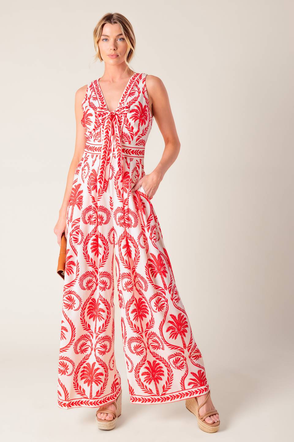 A white and red printed woven jumpsuit featuring V neckline with front tie, sleeveless, wide leg and back zipper closure.