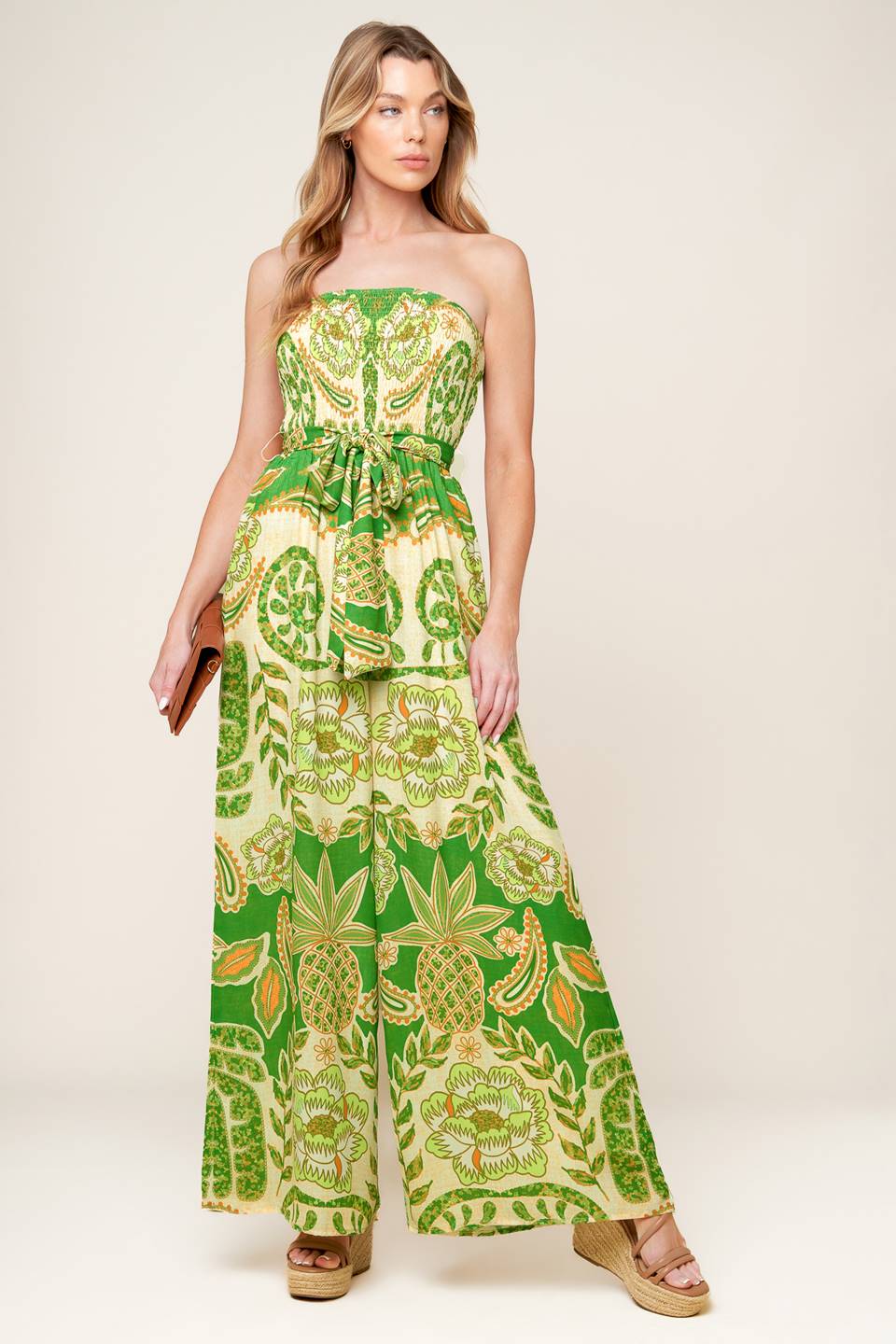 A printed woven jumpsuit featuring strapless, smocked bodice, self sash tie and wide leg