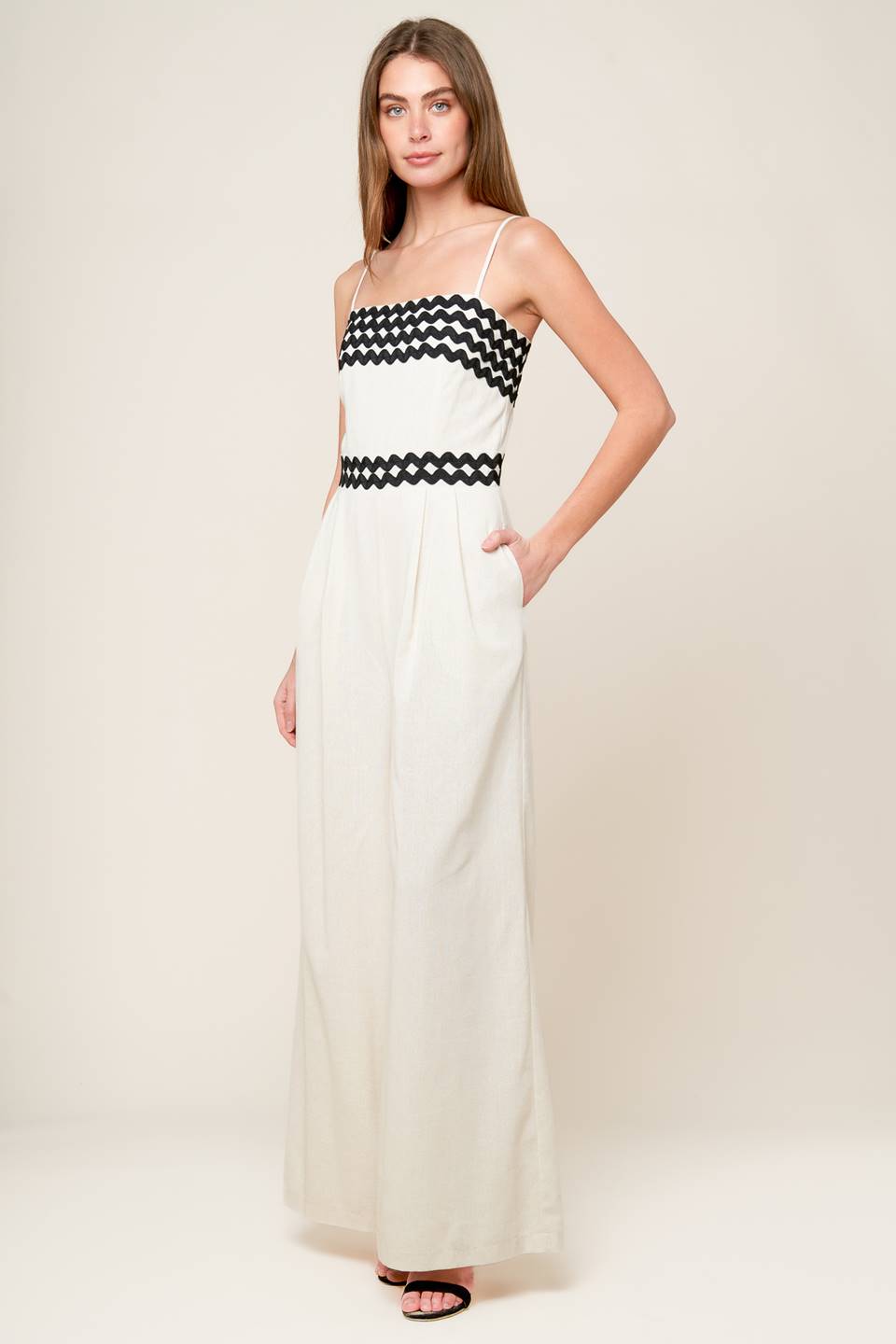 A solid woven jumpsuit featuring straight neckline, straps, ric rac trimmed bodice and waistband, wide leg and back zipper closure.