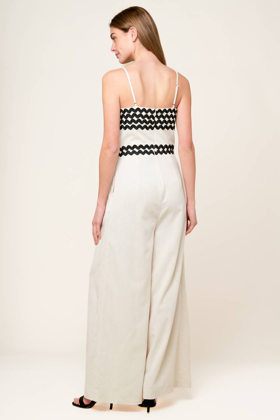 A solid woven jumpsuit featuring straight neckline, straps, ric rac trimmed bodice and waistband, wide leg and back zipper closure.