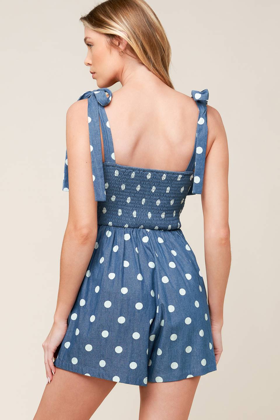 A polka-dotted printed denim romper featuring straight neckline, shoulder tie, side pockets and smocked back bodice.