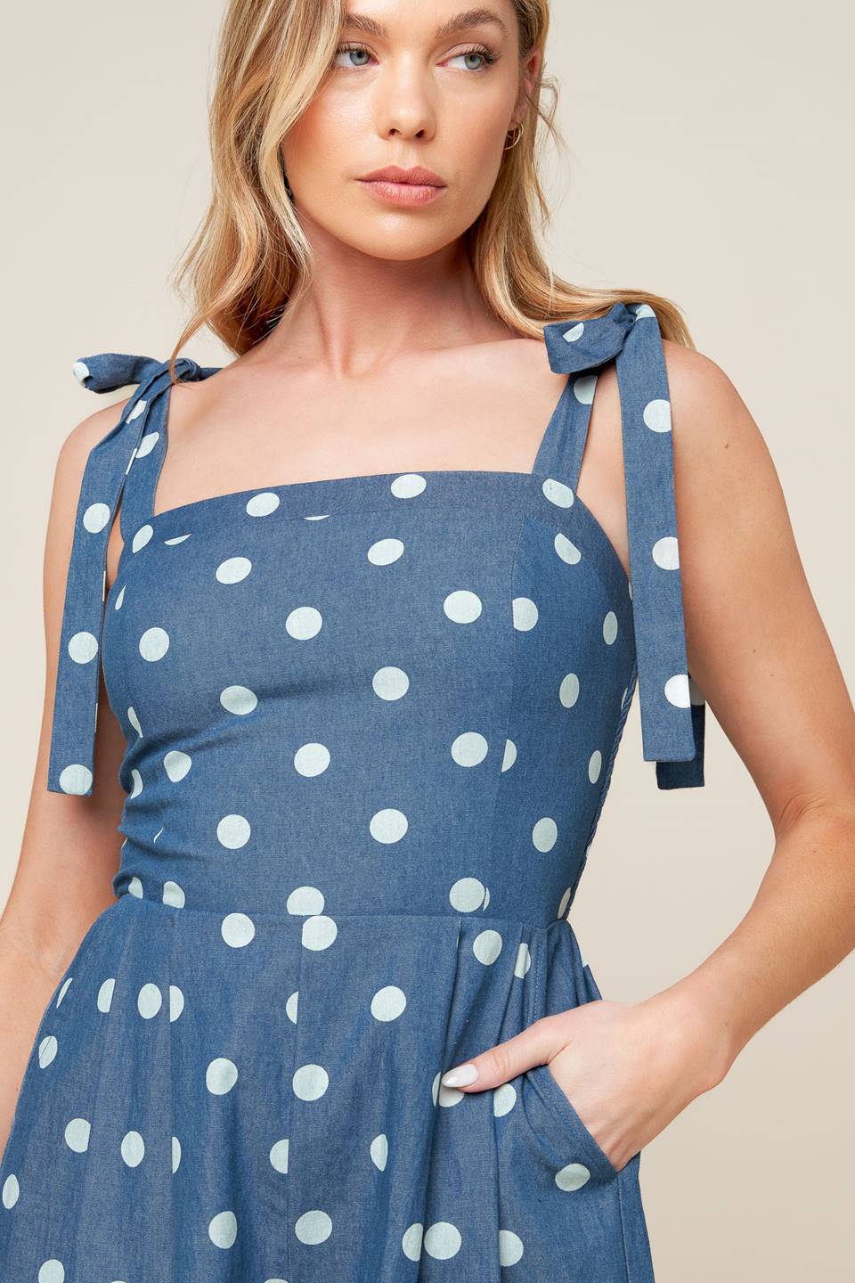 A polka-dotted printed denim romper featuring straight neckline, shoulder tie, side pockets and smocked back bodice.