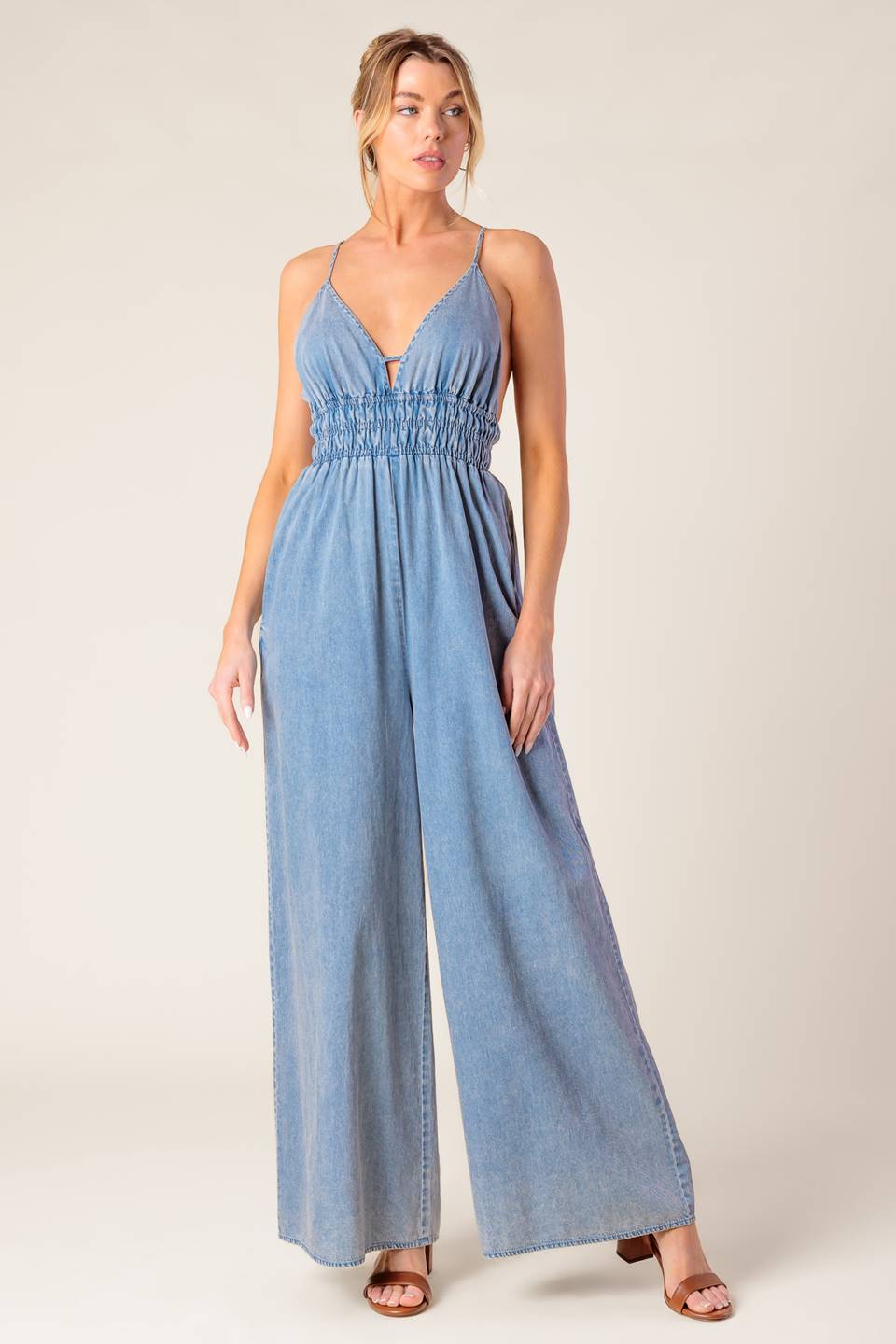 A washed light weight denim jumpsuit featuring V neckline, smocked waist, wide leg and bare back