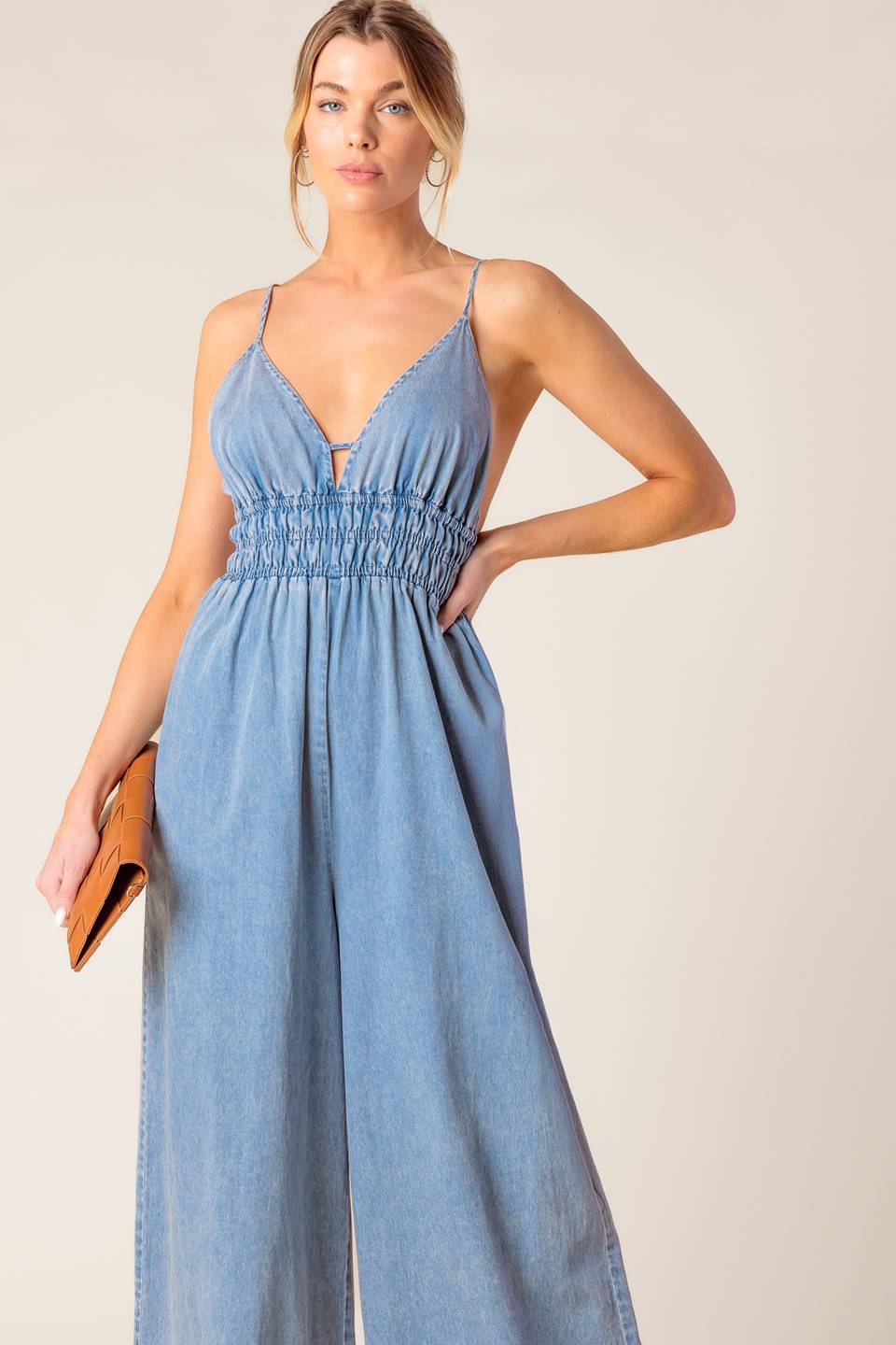 A washed light weight denim jumpsuit featuring V neckline, smocked waist, wide leg and bare back