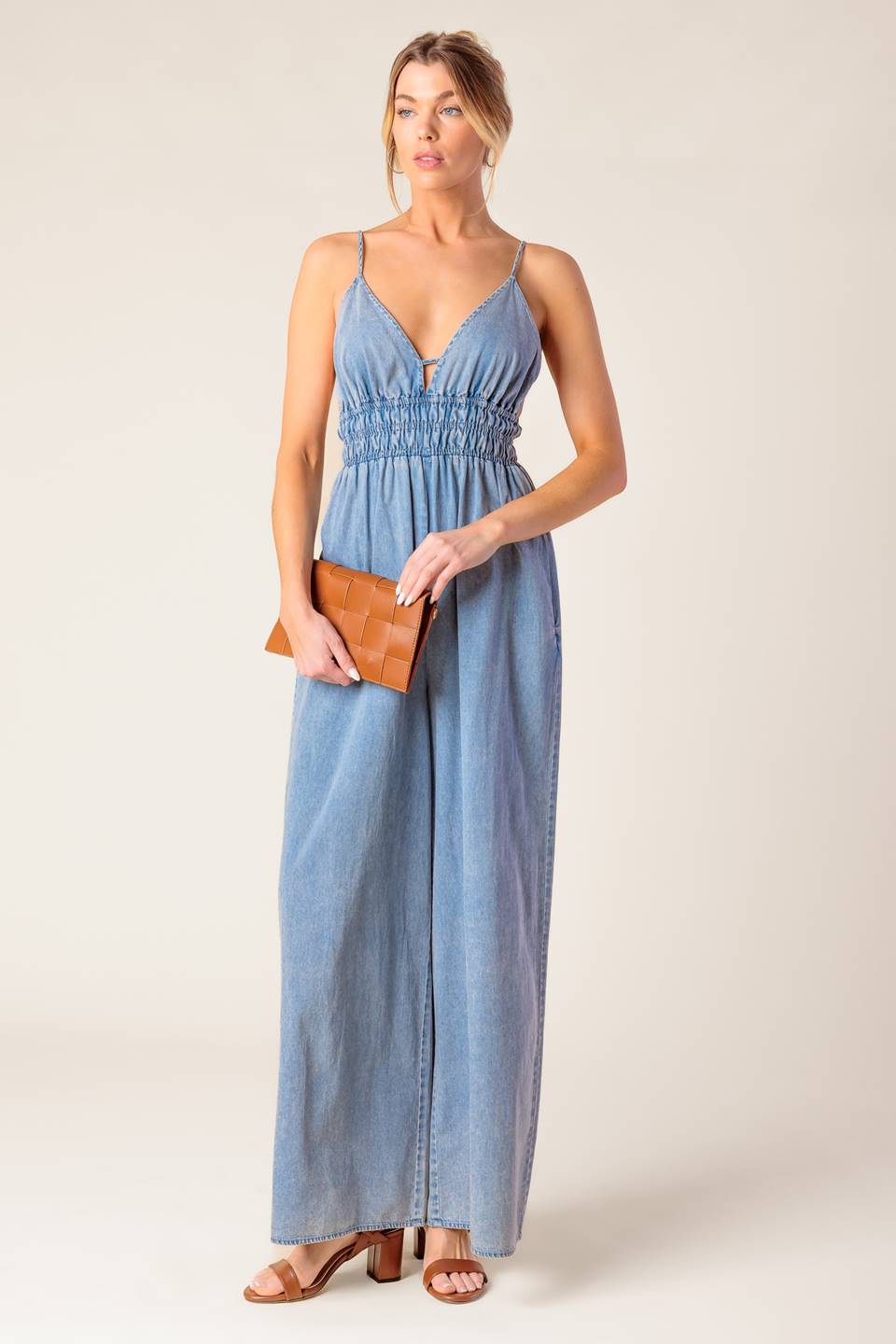 A washed light weight denim jumpsuit featuring V neckline, smocked waist, wide leg and bare back