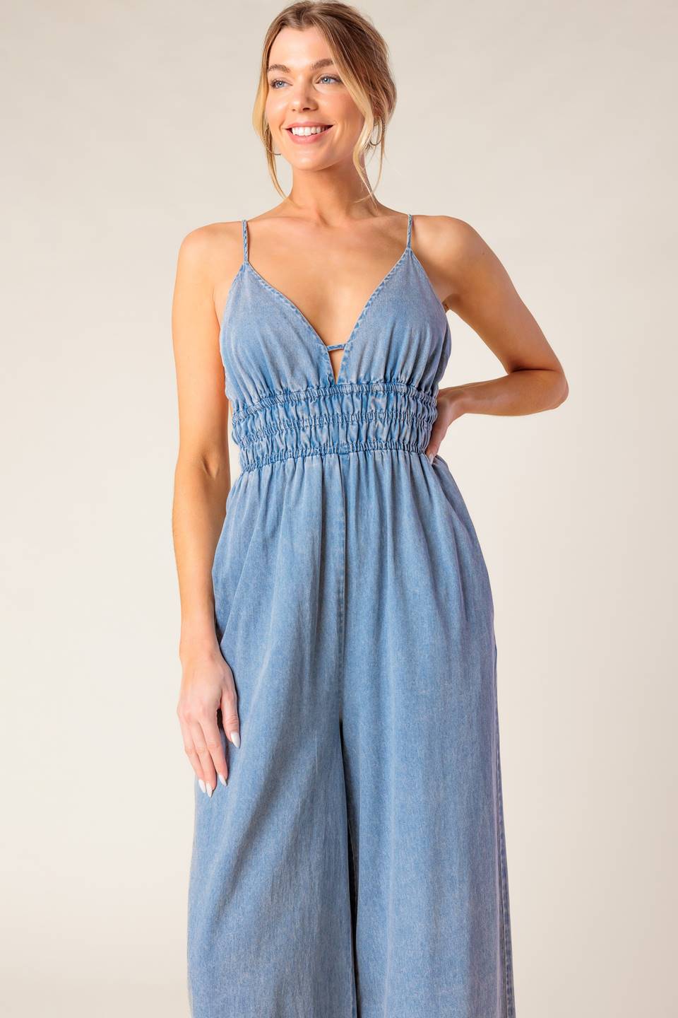 A washed light weight denim jumpsuit featuring V neckline, smocked waist, wide leg and bare back