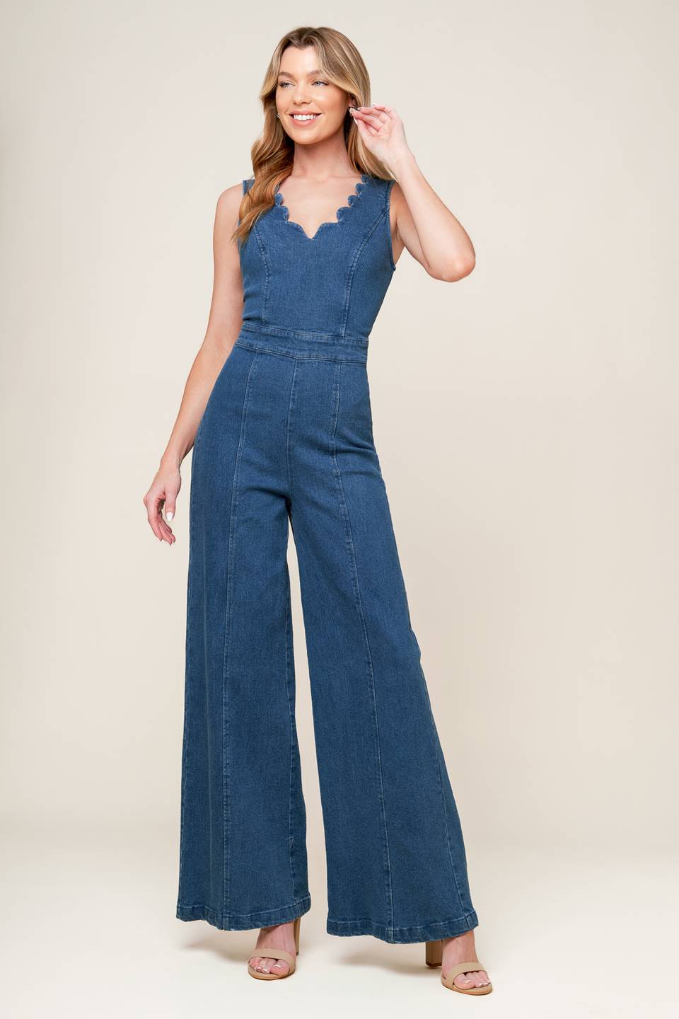 A washed denim jumpsuit featuring scalloped V neckline, sleeveless, self sash belt, wide leg and back zipper closure.