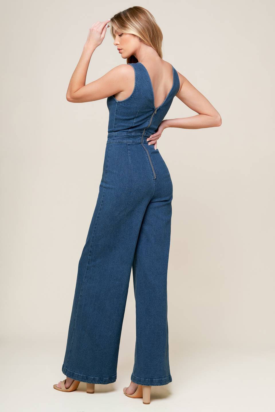 A washed denim jumpsuit featuring scalloped V neckline, sleeveless, self sash belt, wide leg and back zipper closure.