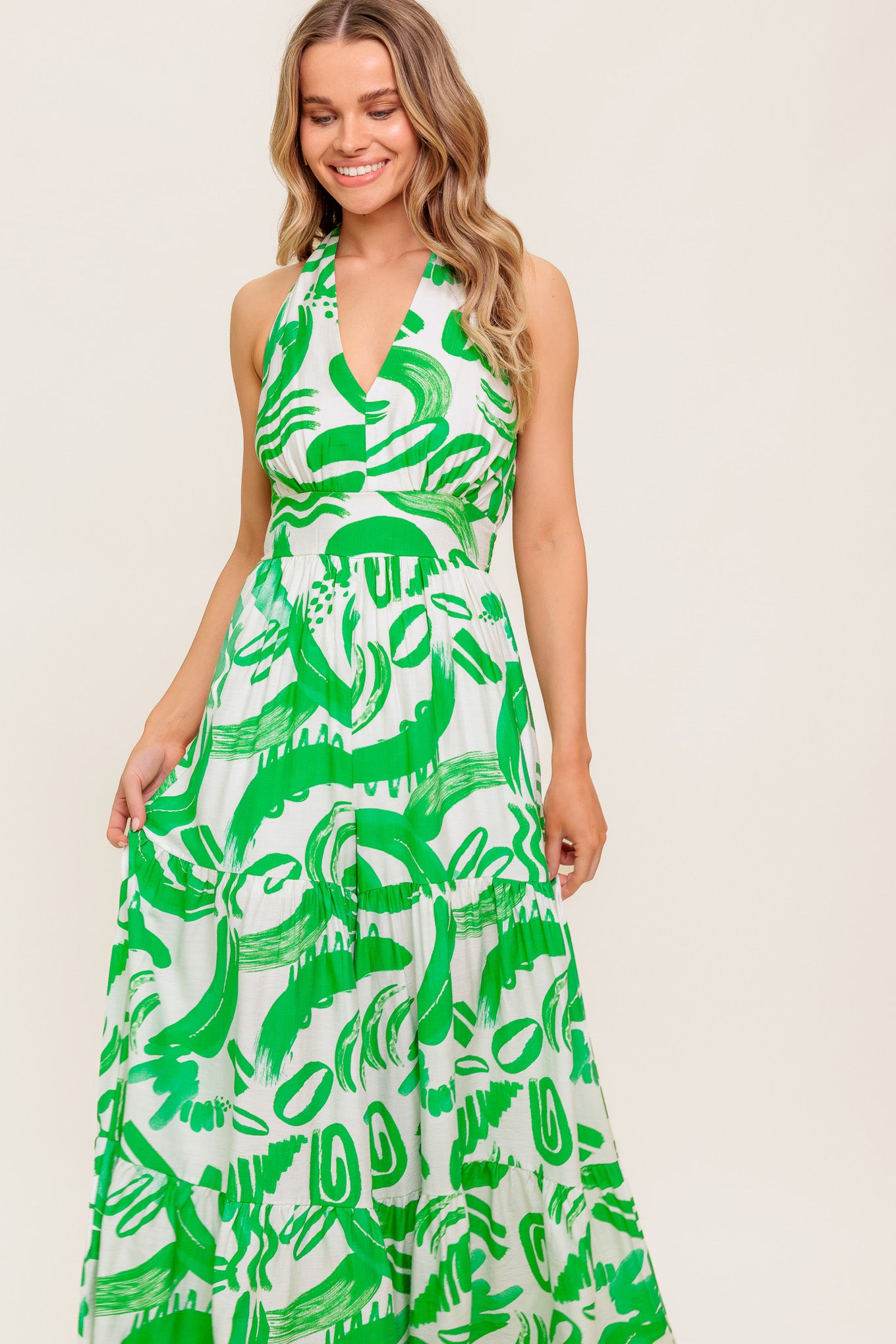 A printed woven jumpsuit featuring halter neckline, tiered pant, bare back with tie and smocked back waistband