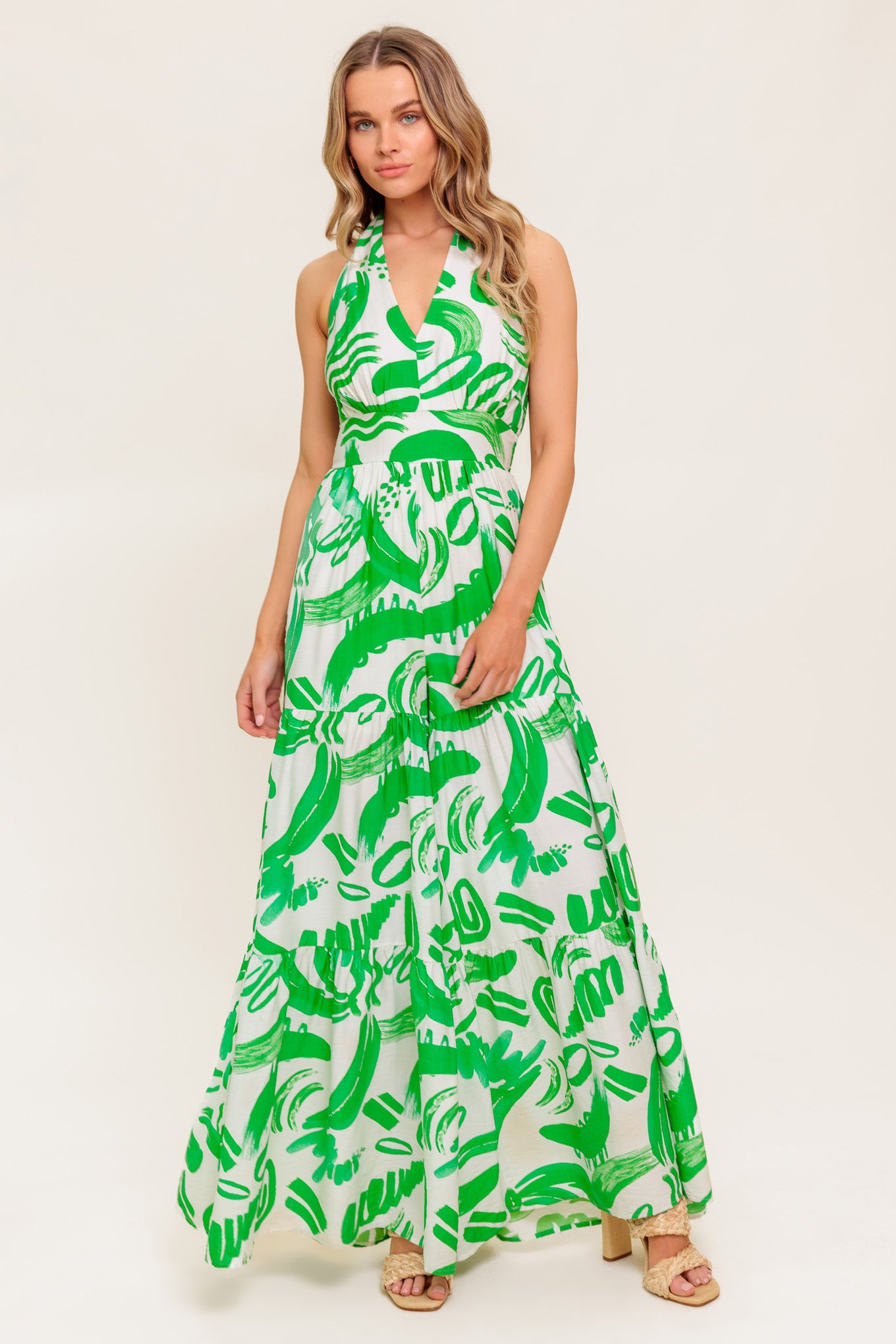 A printed woven jumpsuit featuring halter neckline, tiered pant, bare back with tie and smocked back waistband