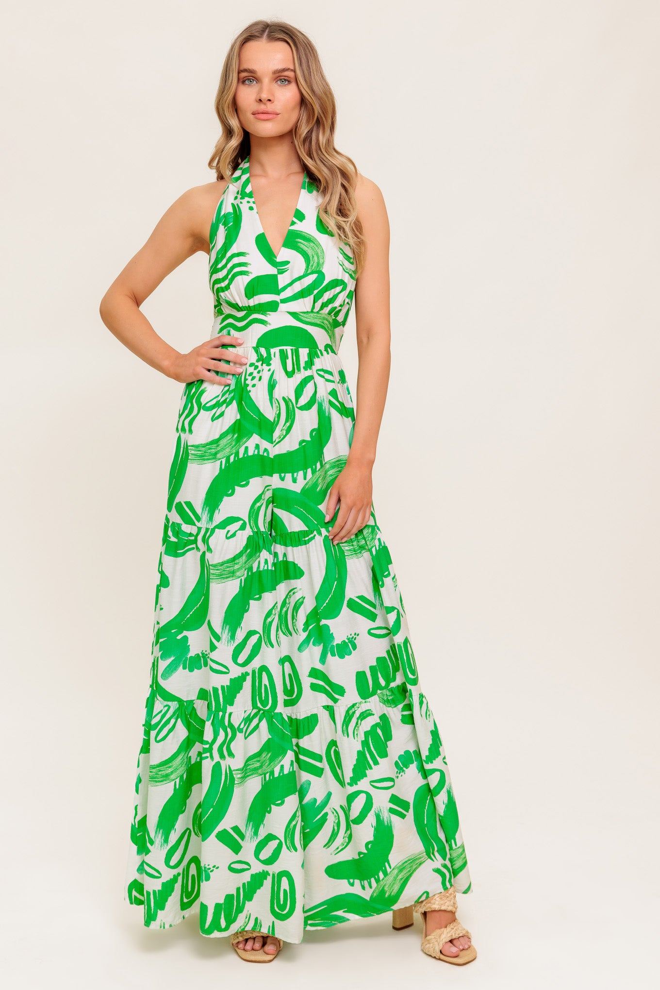 A printed woven jumpsuit featuring halter neckline, tiered pant, bare back with tie and smocked back waistband
