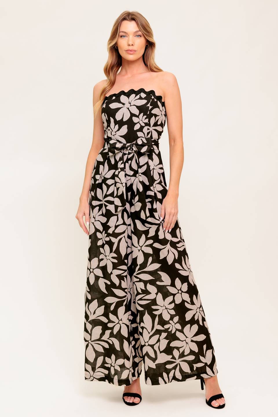 A printed woven jumpsuit featuring strapless neckline with ric rac trimmed edge, self sash tie, wide leg and back zipper closure.