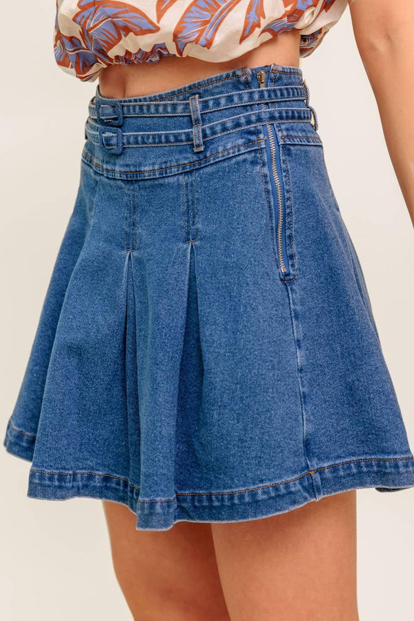 A washed denim skort featuring double self belt, inverted pleats and side zipper closure