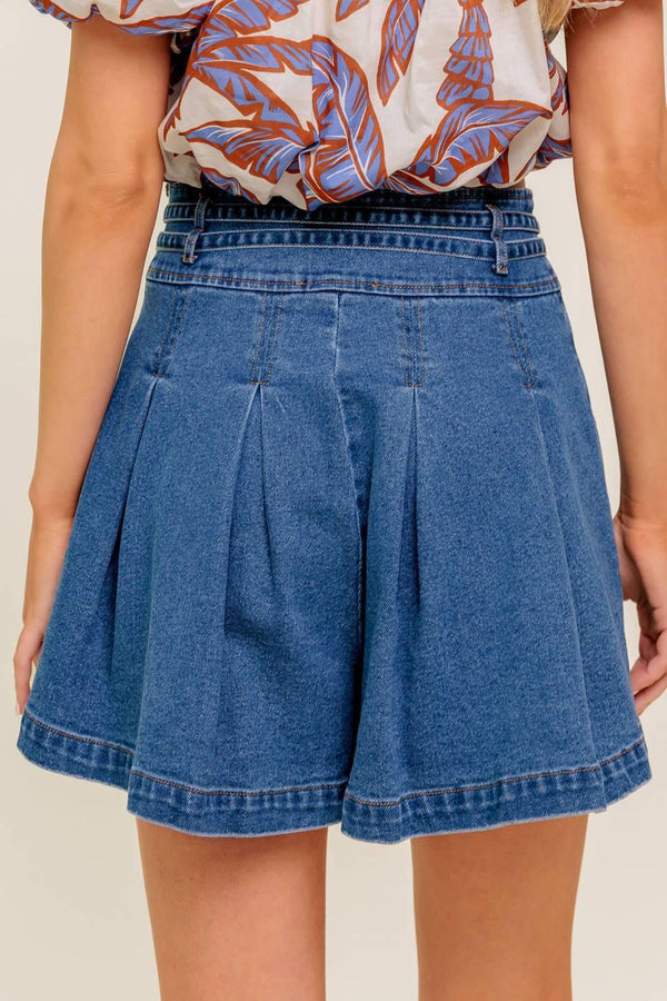 A washed denim skort featuring double self belt, inverted pleats and side zipper closure