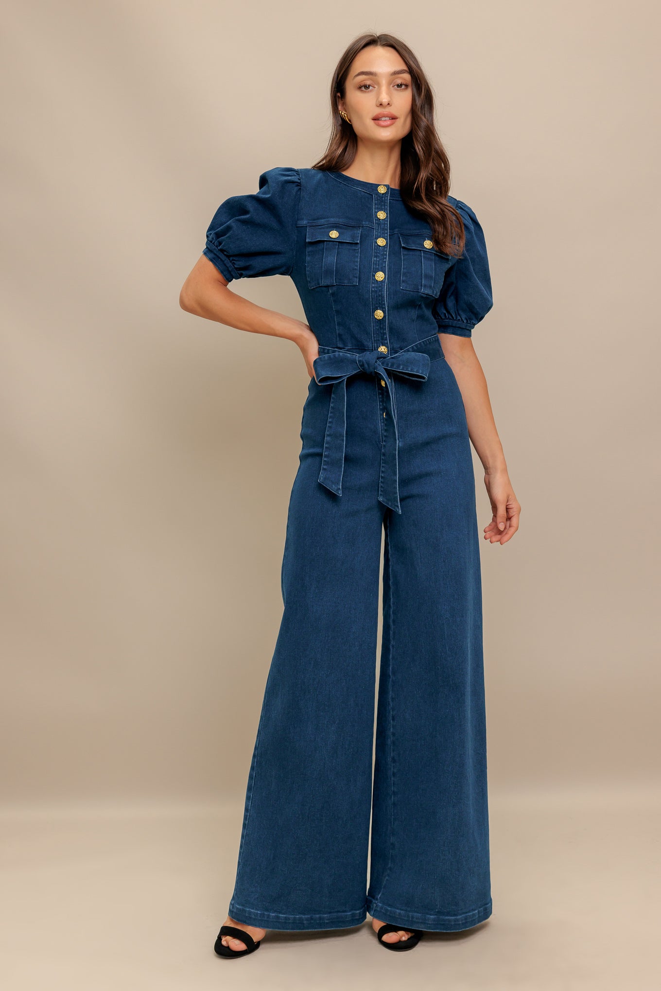 A washed denim jumpsuit featuring round neckline, short puff sleeve, front pockets, button down, self belt and wide leg