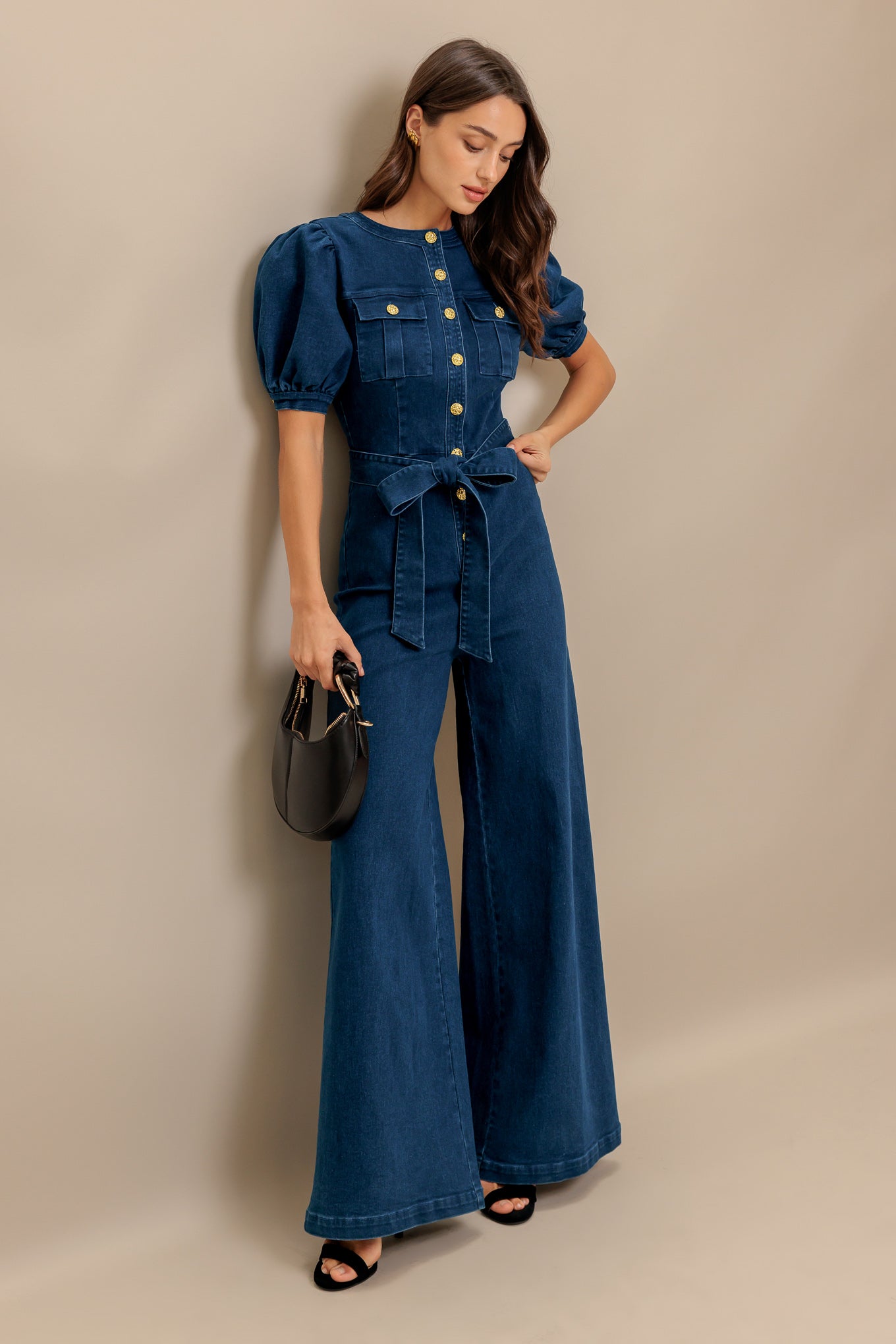 A washed denim jumpsuit featuring round neckline, short puff sleeve, front pockets, button down, self belt and wide leg