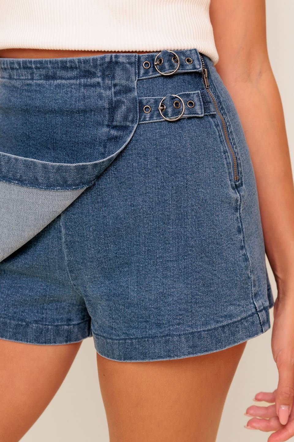 A washed denim skort featuring side buckle detail and zipper closure.