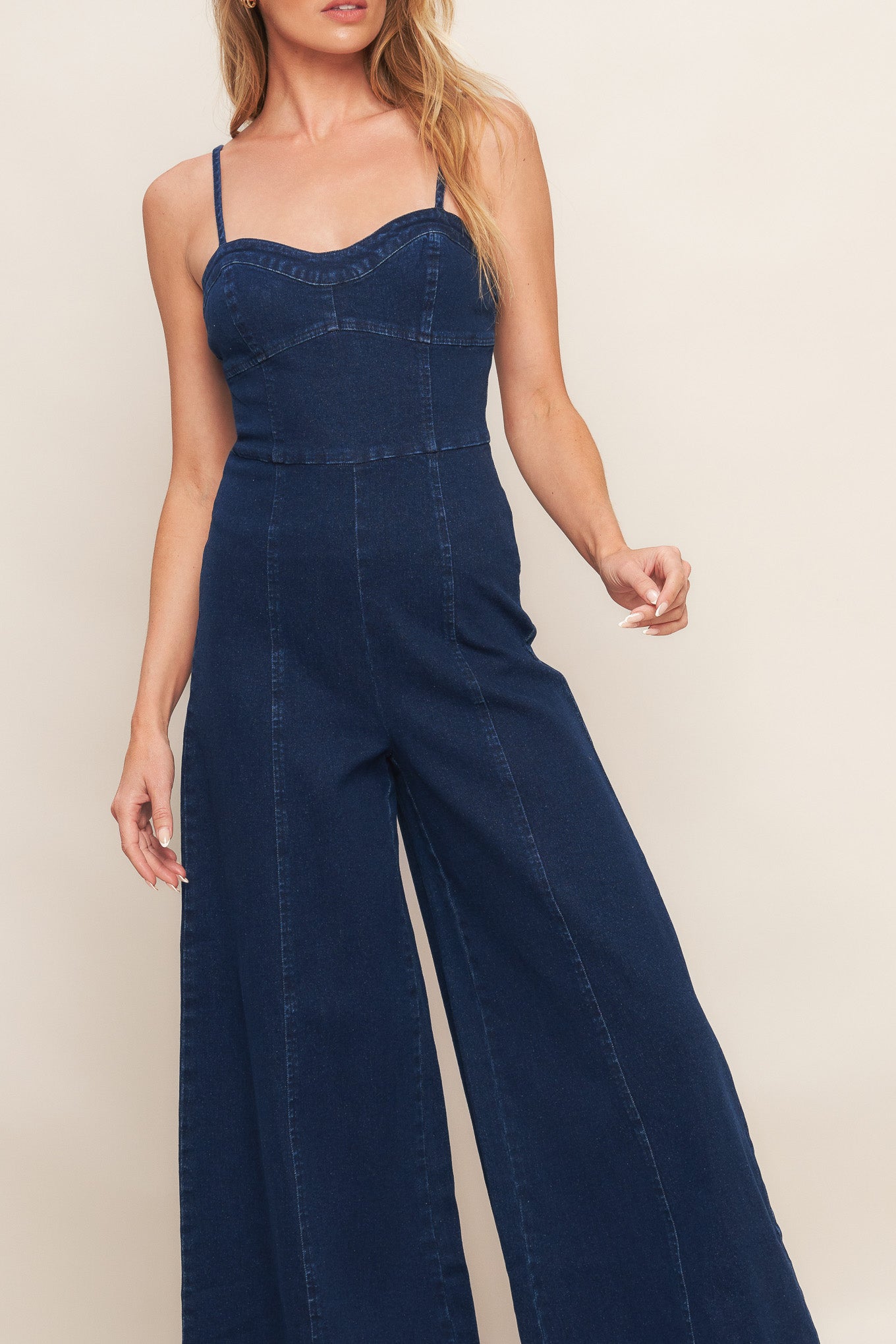 A washed denim jumpsuit featuring bustier top with straps, side leg and back zipper closure