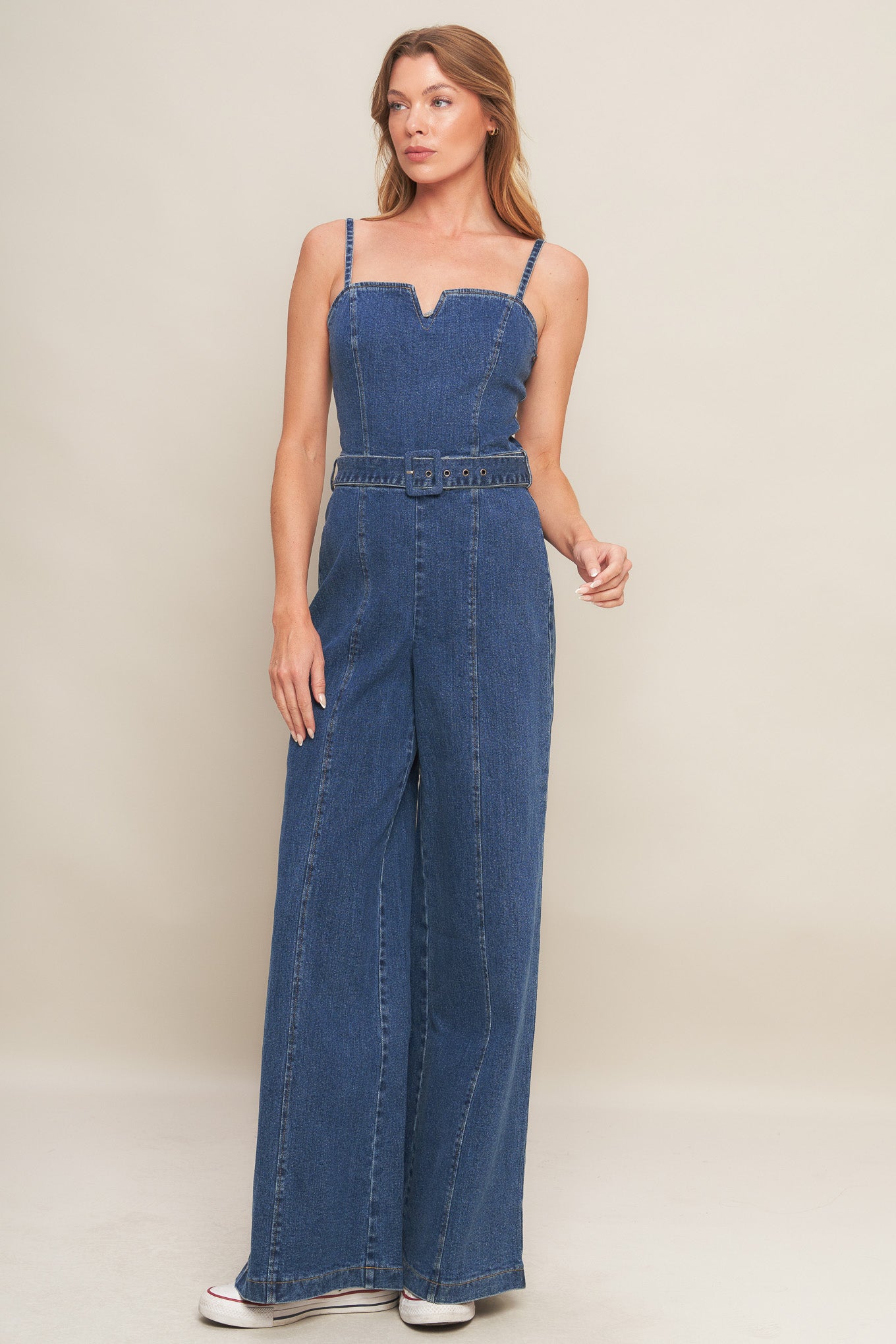 A washed denim jumpsuit featuring straight neckline with V cut out, straps, self belt, wide leg and back zipper closure