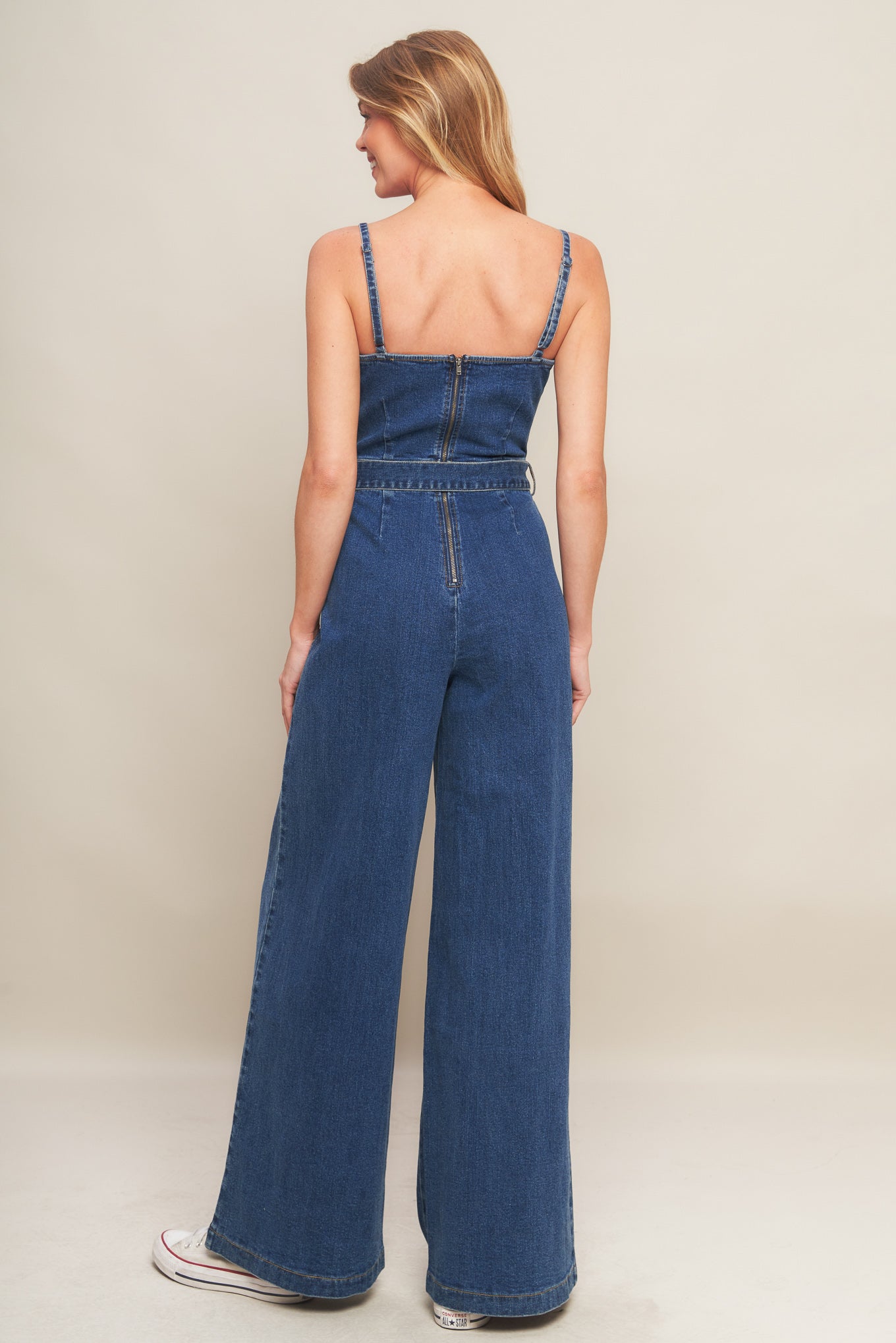 A washed denim jumpsuit featuring straight neckline with V cut out, straps, self belt, wide leg and back zipper closure