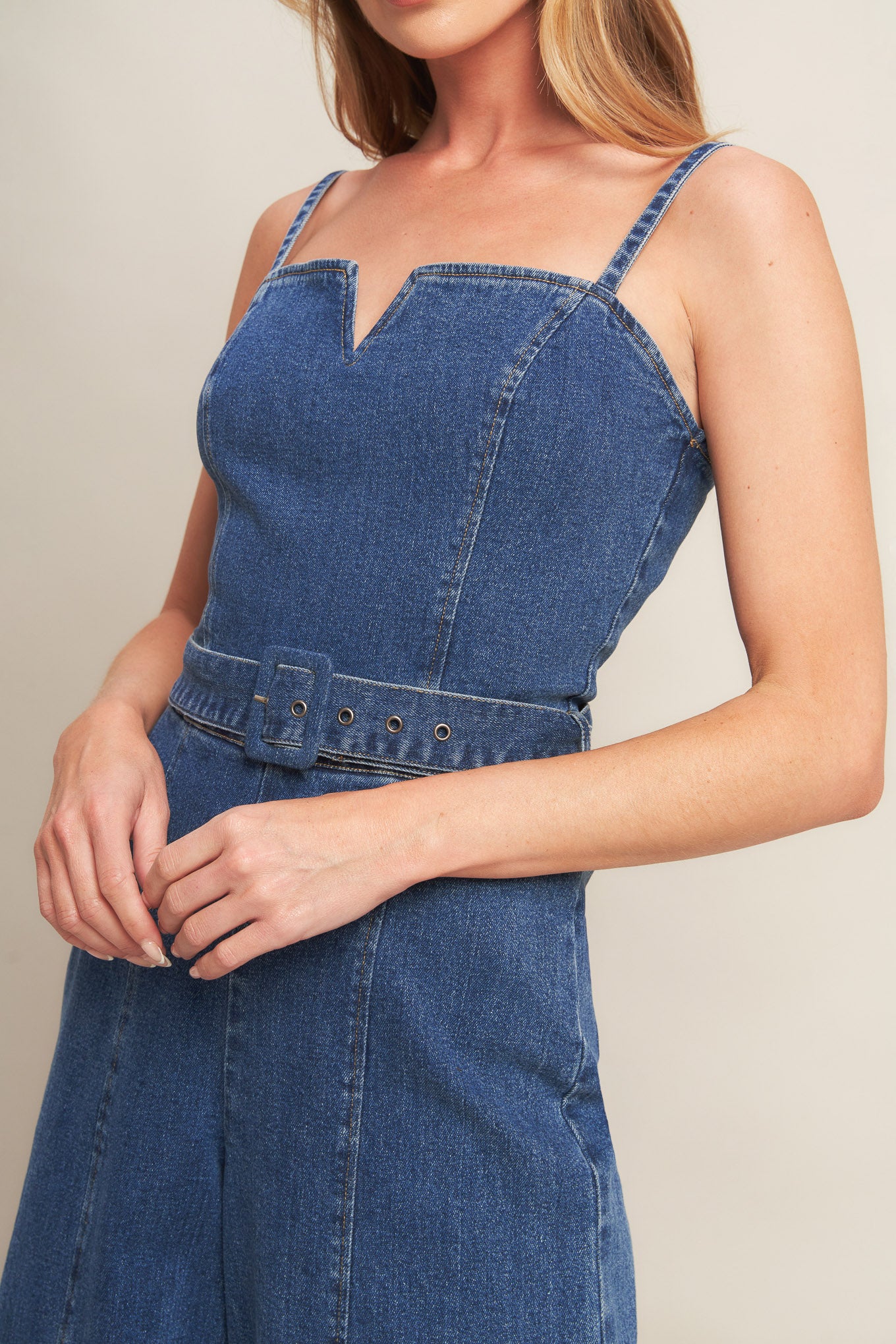 A washed denim jumpsuit featuring straight neckline with V cut out, straps, self belt, wide leg and back zipper closure