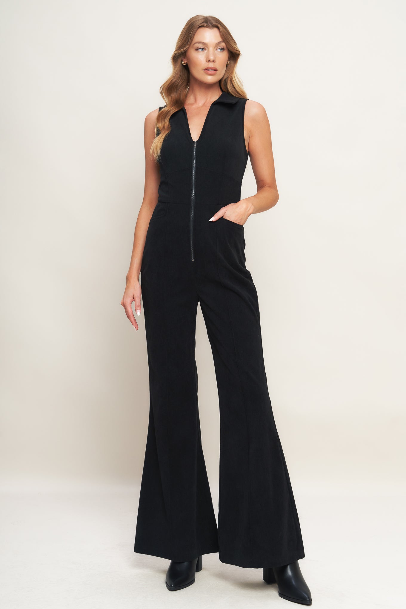 A solid corduroy jumpsuit featuring collar, V neckline, sleeveless, front zipper, waist yoke, side pocket and flare leg